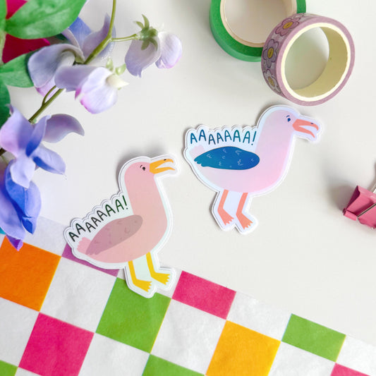 An image showing two holographic stickers of seagulls, one in pink one in more life-like colours. The text reads 'AAAAAAA!' as if the seagulls are screaming.