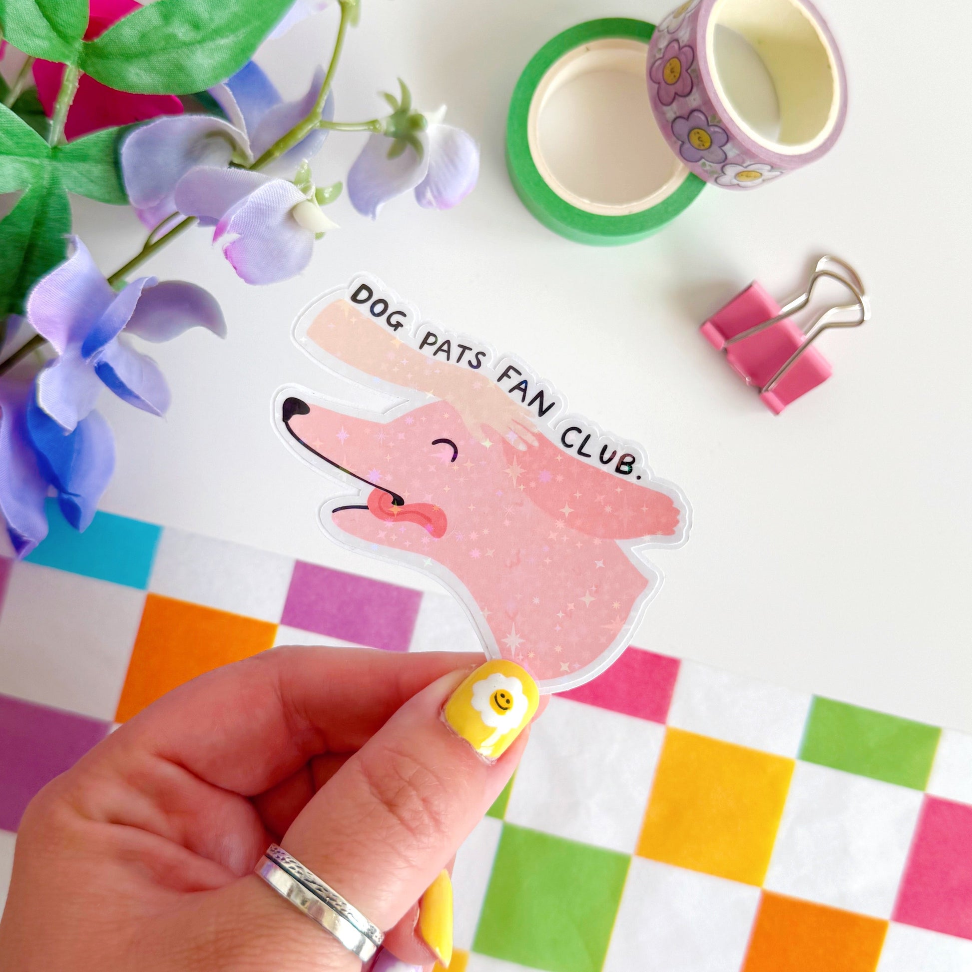 A holographic sticker of a pink dog, with its tongue sticking out, with a hand patting its head. The text reads 'Dog Pats Fan Club.'