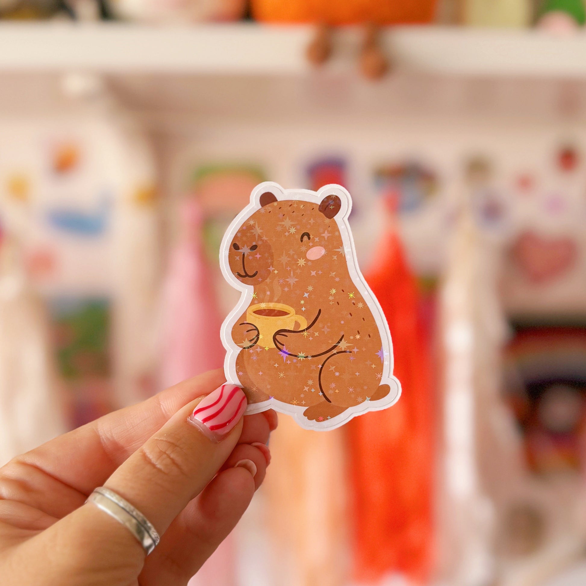 Hand holding a cute animal sticker with a blurred background of colorful items