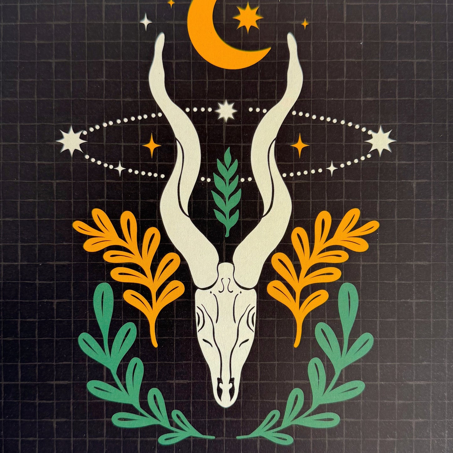 Decorative print with a deer skull, crescent moon, and foliage on a grid background
