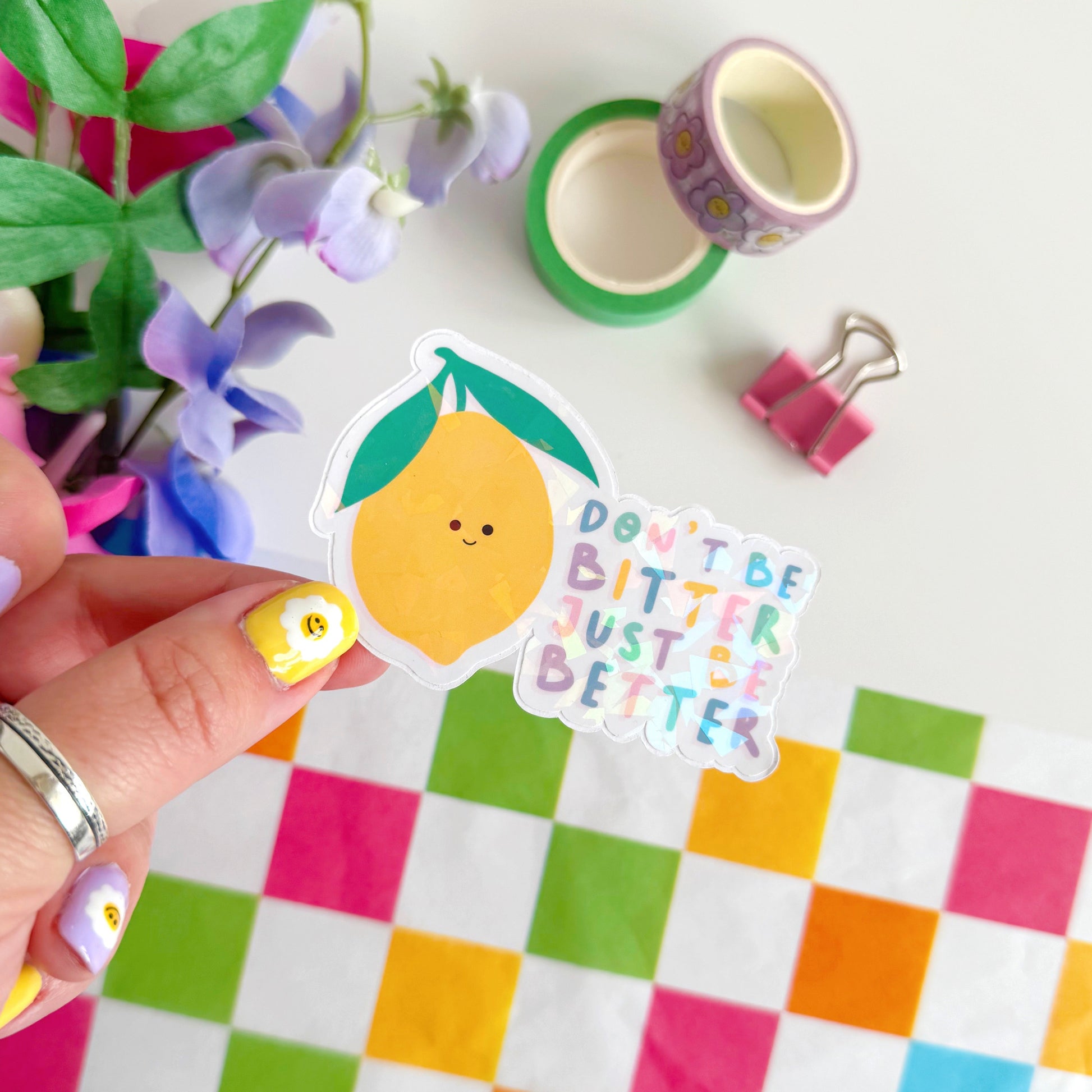 A holographic sticker, of a smiling lemon and the quote don't be bitter just be better. The sticker has an easy peel lip.
