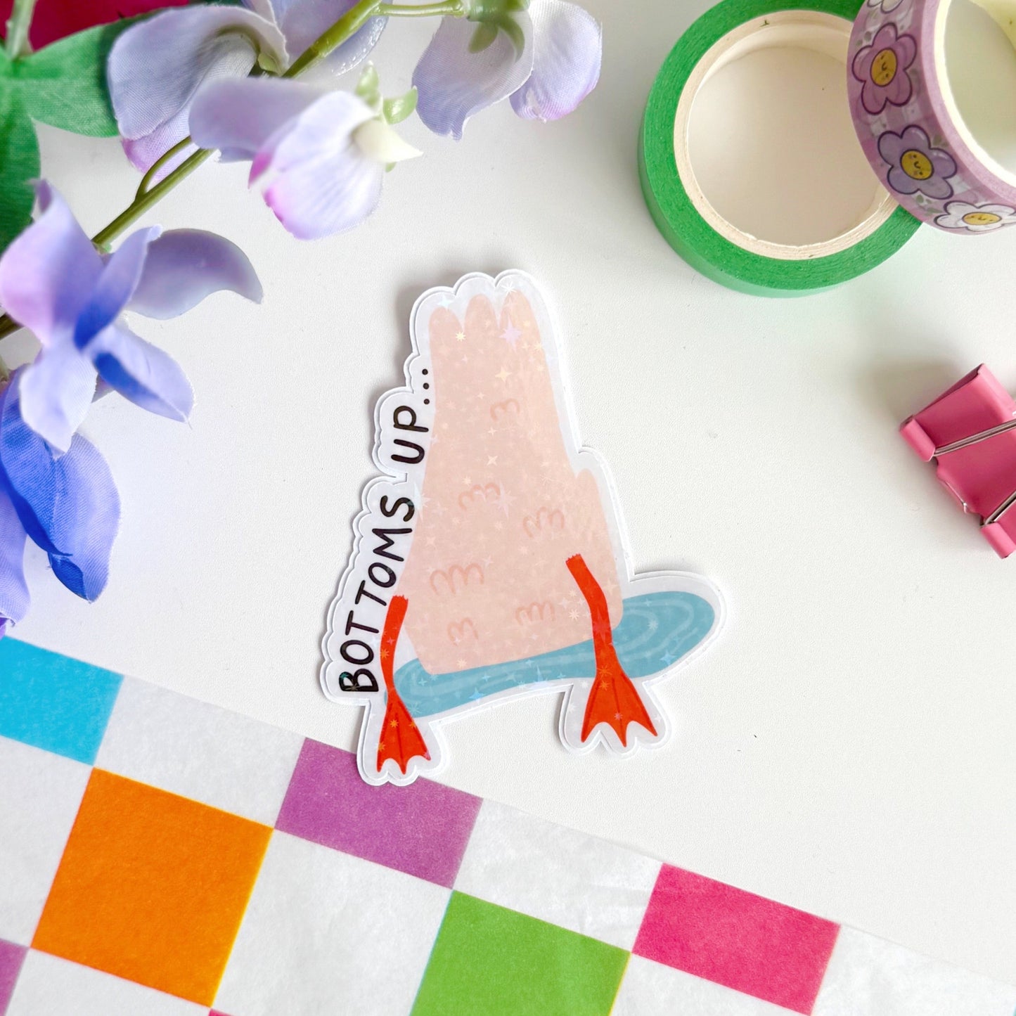 A holographic sticker of a duck upside down in water, with the text - bottoms up, next to it.