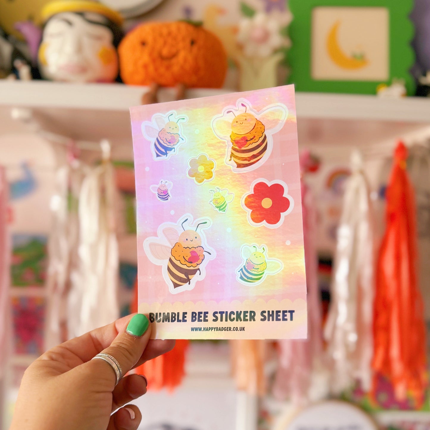 Hand holding a sticker sheet with colourful bumble bee designs in front of a shelf.