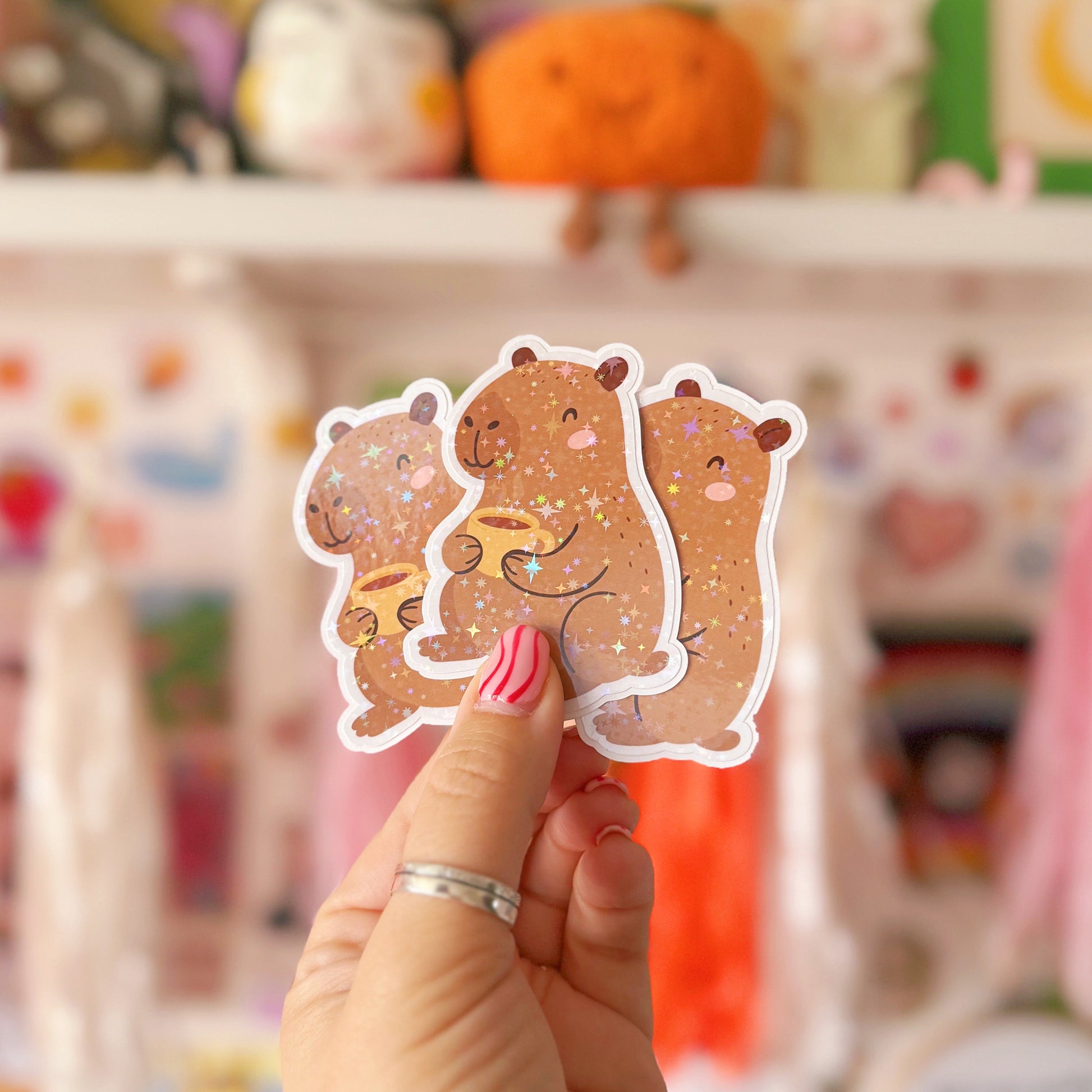 Hand holding a cute animal sticker with a blurred background of colourful items
