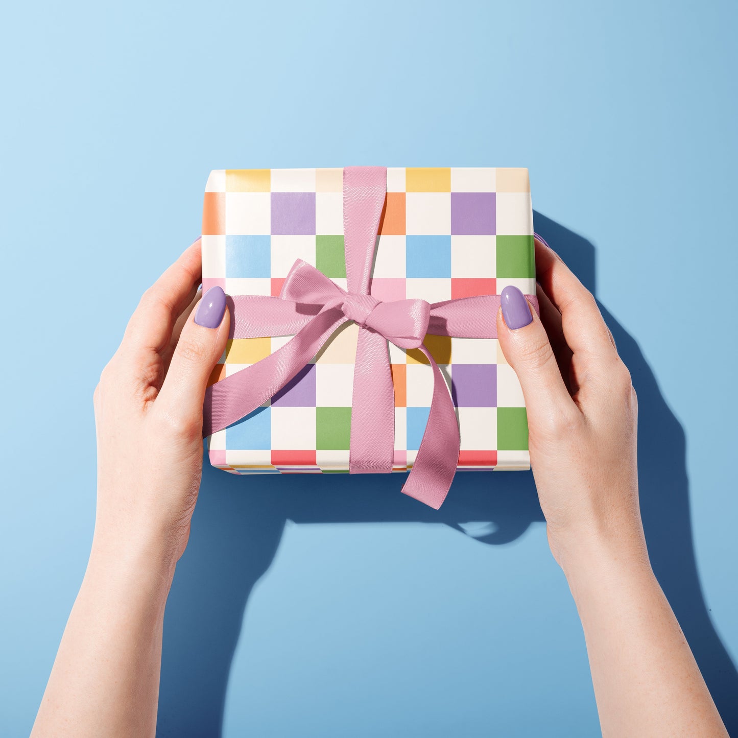 A multicoloured checkerboard pattern gift wrap, shown wrapped around a gift with blue ribbon.