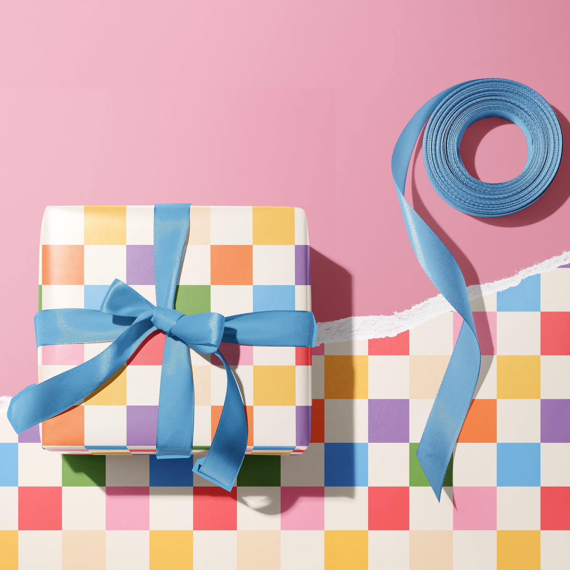 A multicoloured checkerboard pattern gift wrap, shown wrapped around a gift with blue ribbon.