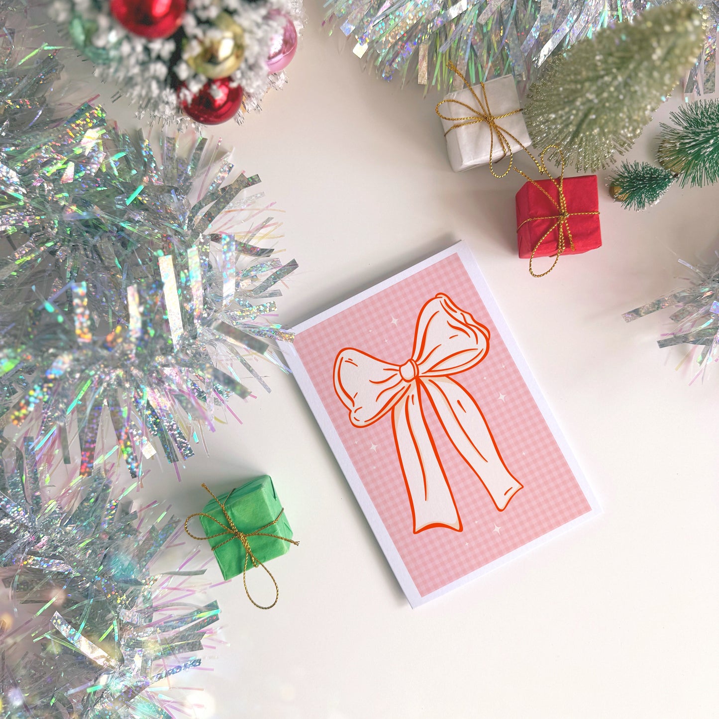 Card with a bow design surrounded by Christmas decorations on a white surface