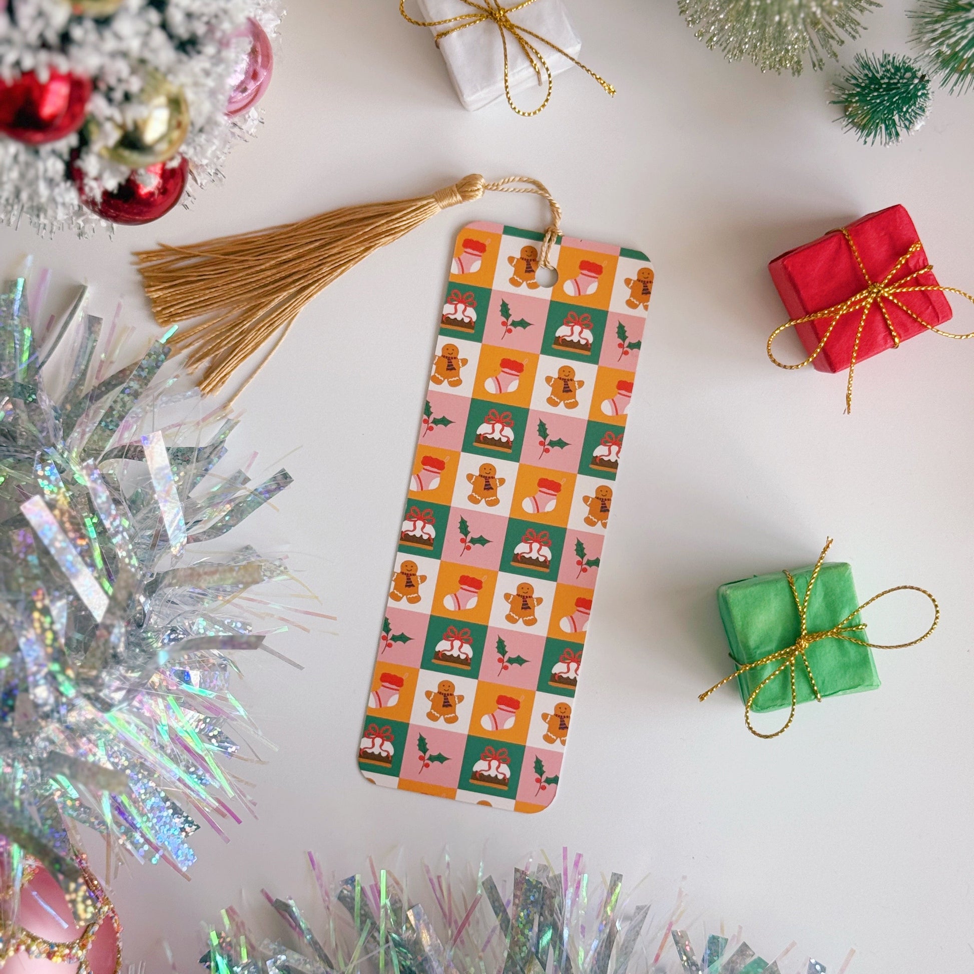A christmas bookmark with a festive pattern surrounded by Christmas decorations on a white surface