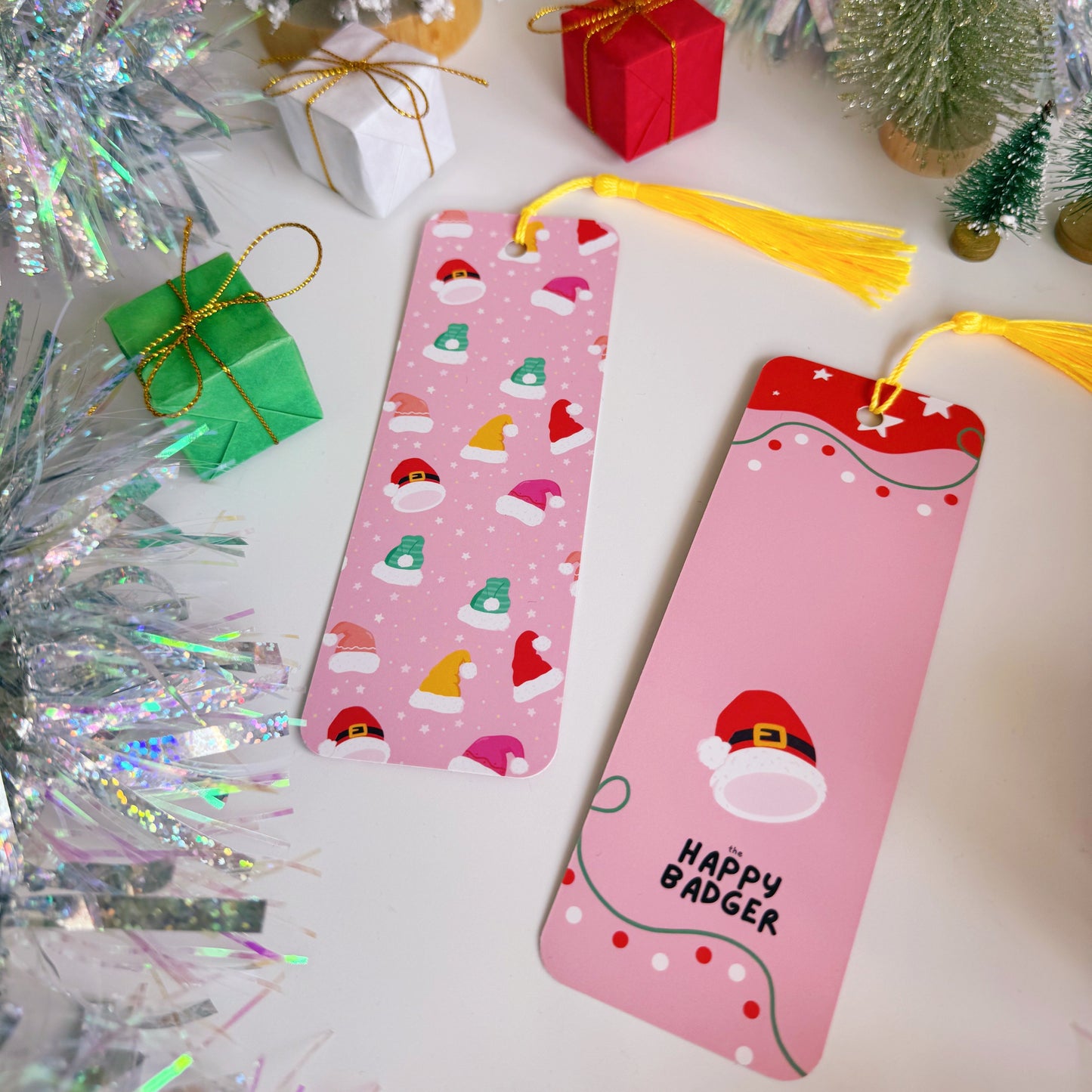 Two pink phone cases with festive designs on a decorative background with Christmas trees and tinsel.