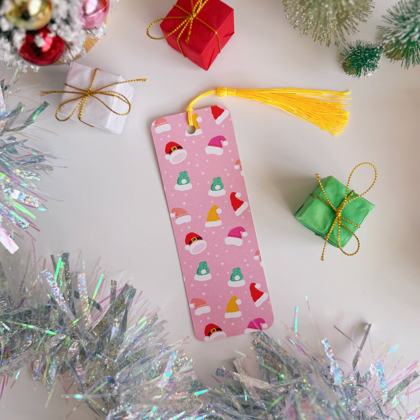 Pink bookmark with Christmas patterns surrounded by festive decorations on a white surface