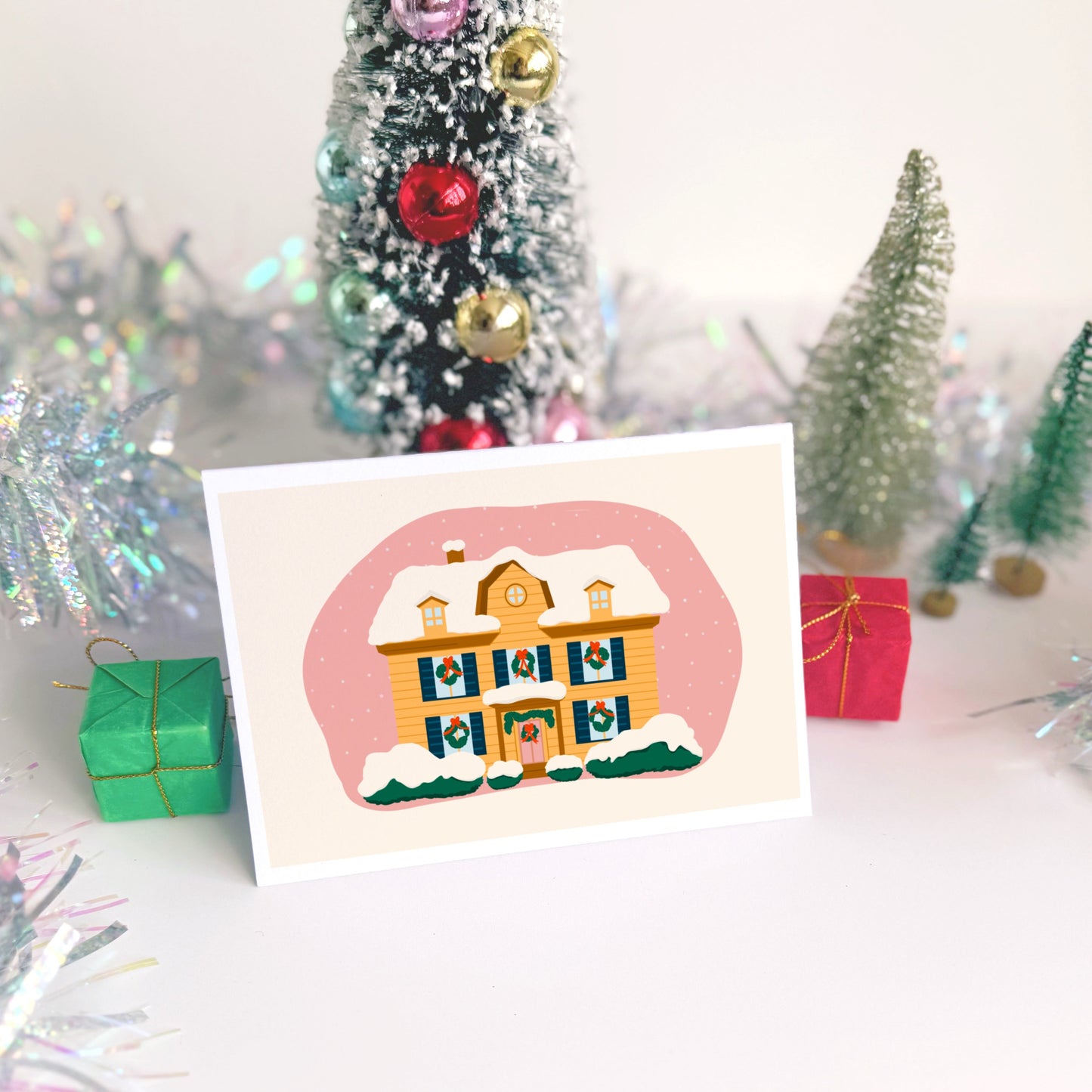 A christmas card with an illustration of a house, decked out with wreaths and covered in snow.