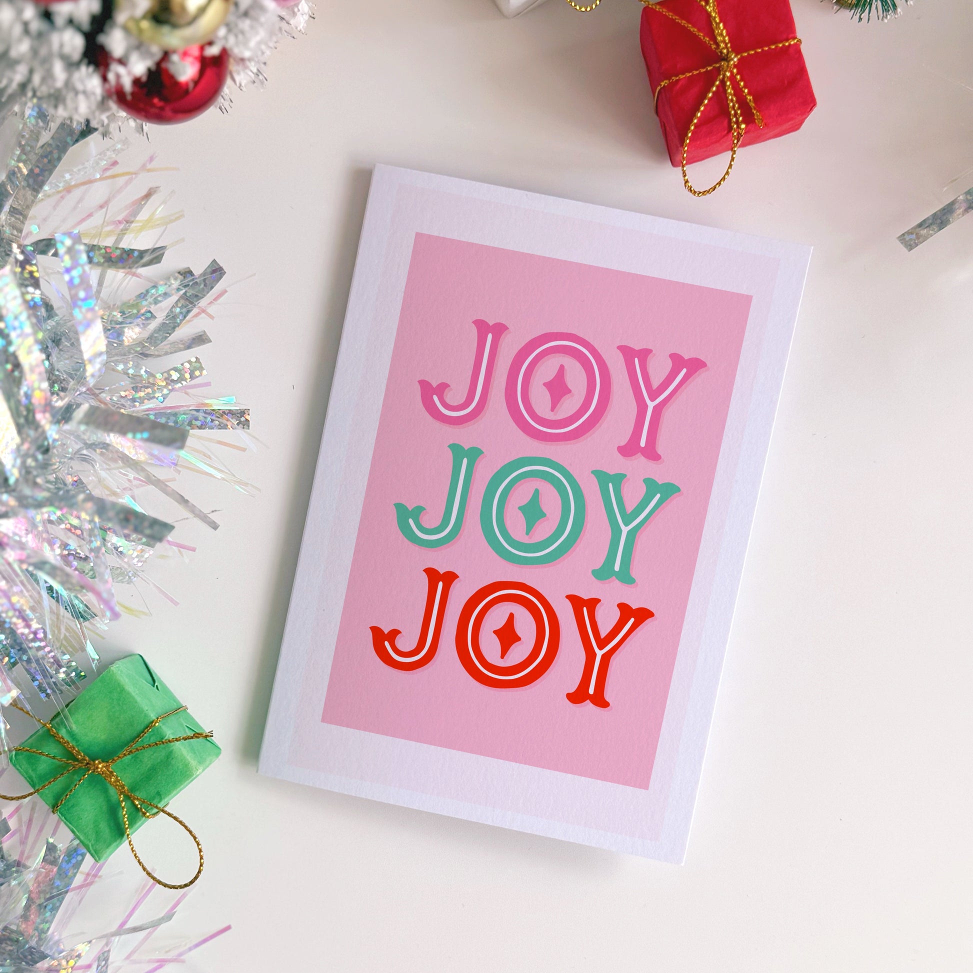 Card with 'JOY JOY JOY' text on a pink background, surrounded by Christmas decorations.