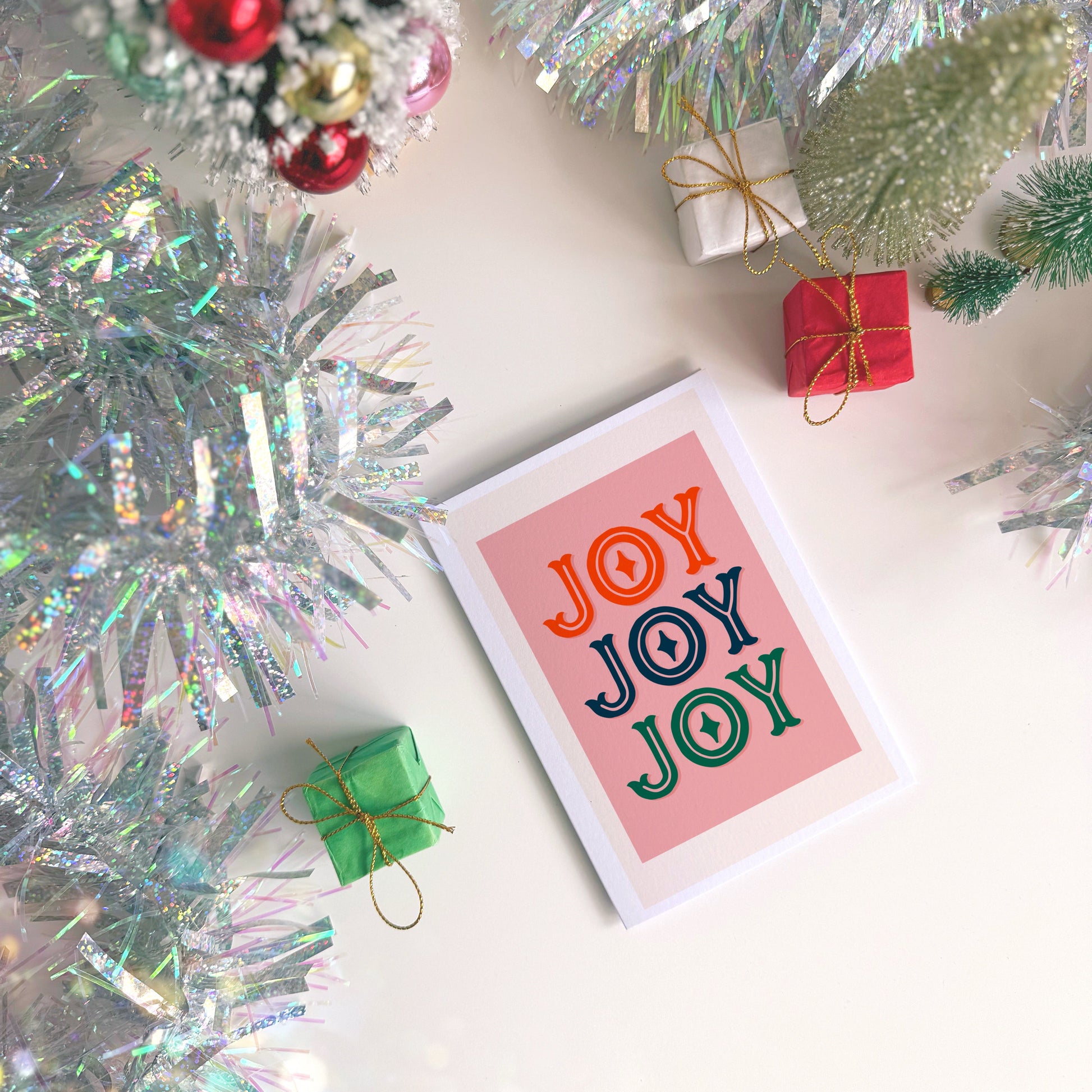 Card with 'JOY JOY JOY' text surrounded by Christmas decorations on a white surface