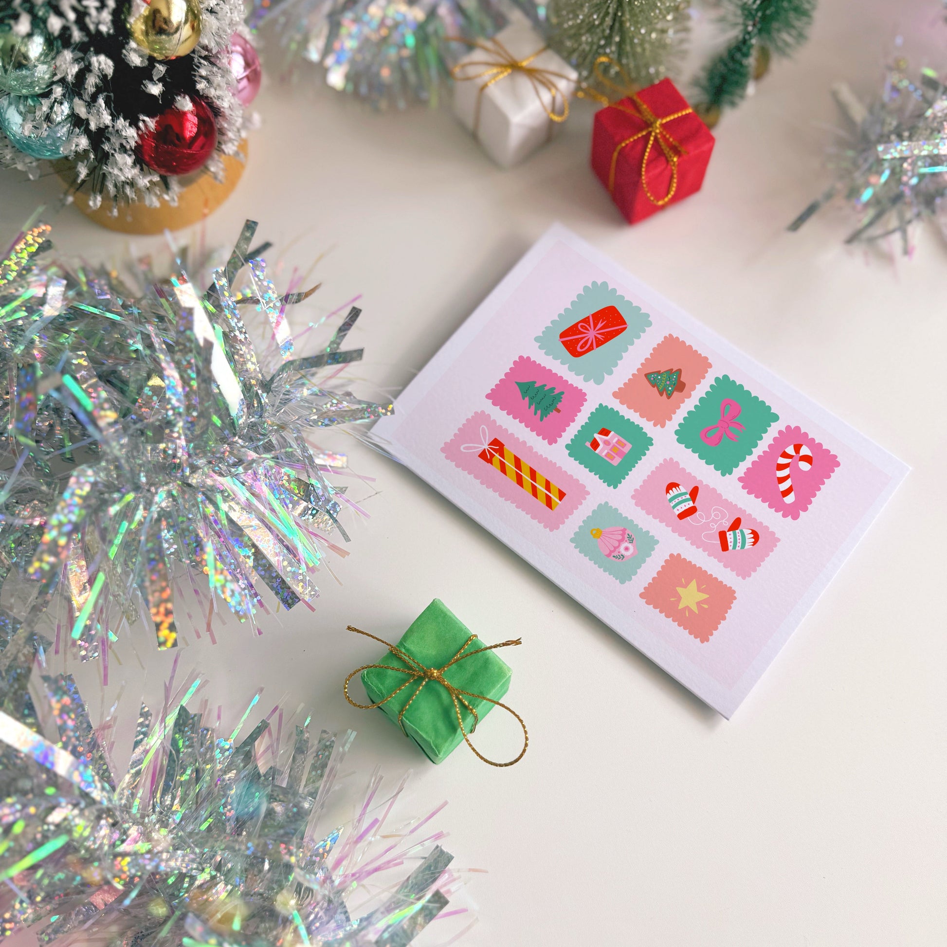 Christmas card with festive designs surrounded by small trees and decorations on a white surface.