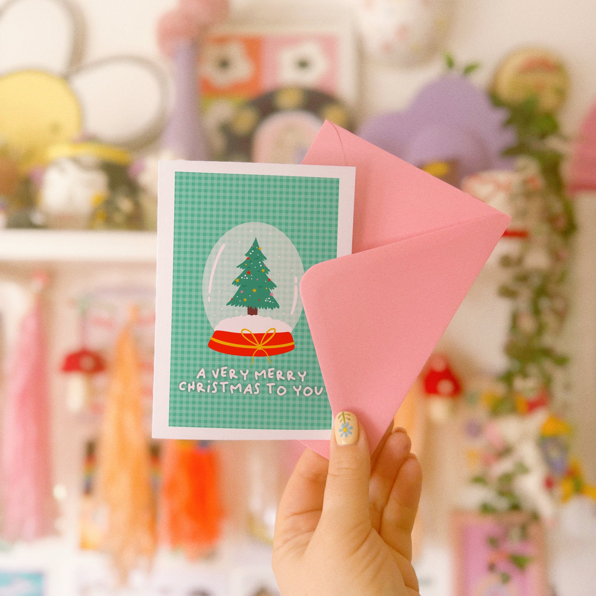 Hand holding a Christmas card with a tree design in front of a colourful background