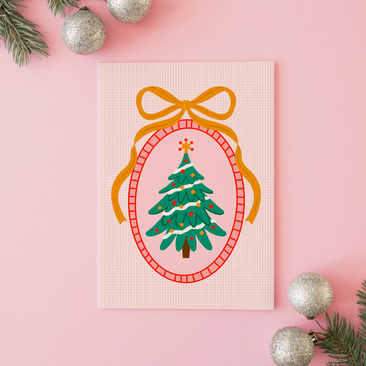 An illustration of a Christmas tree, surrounded by a hand drawn border with a large golden bow on top. The background of the print is a warm pink gingham.