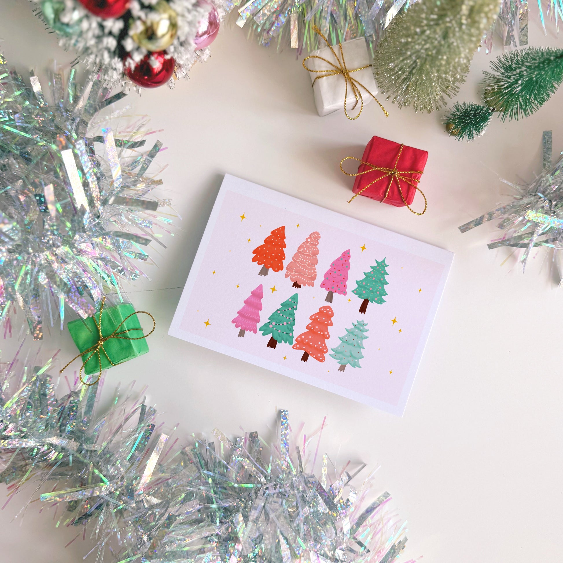 Christmas card with colorful trees surrounded by festive decorations on a white surface