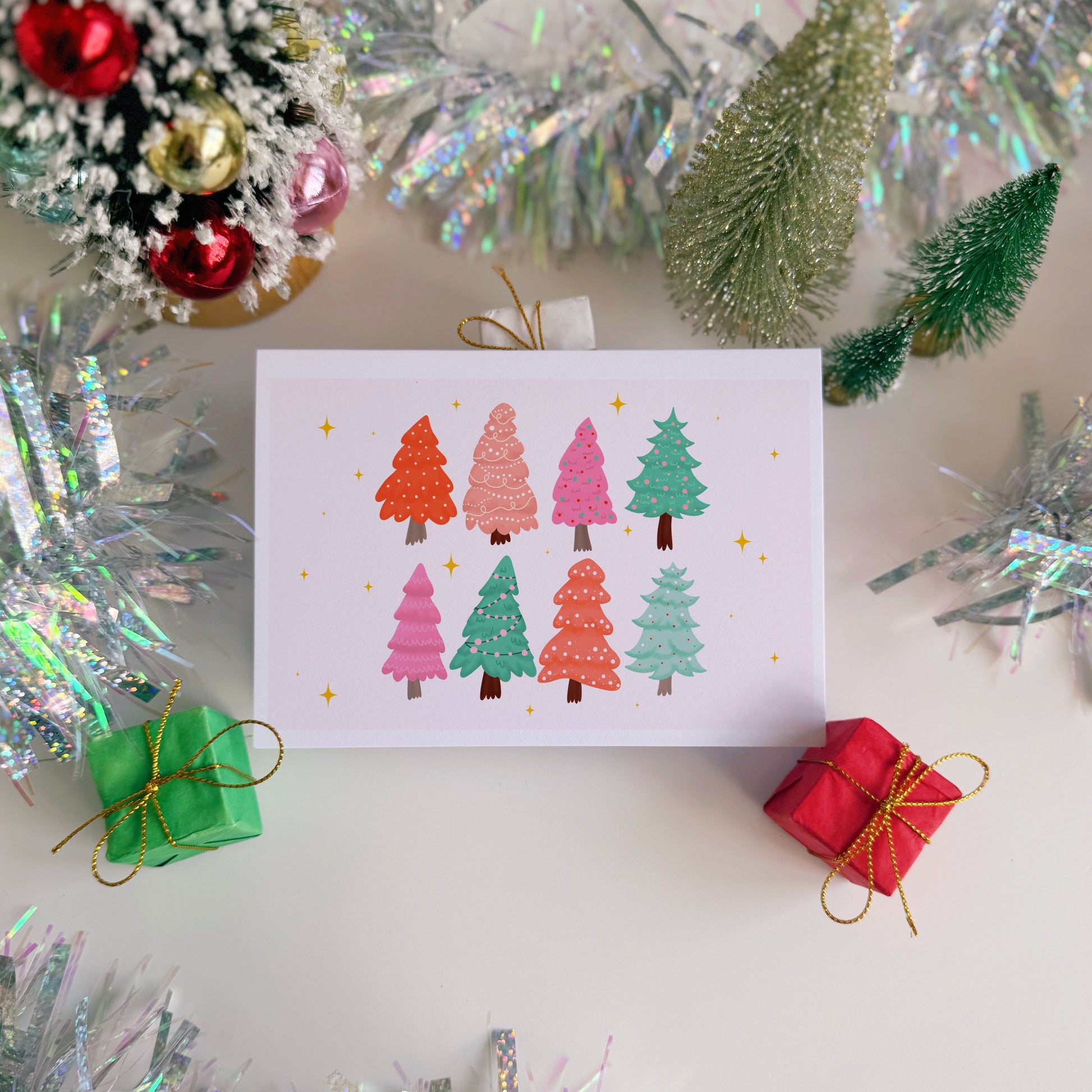 Card with colorful Christmas tree design surrounded by festive decorations on a white surface
