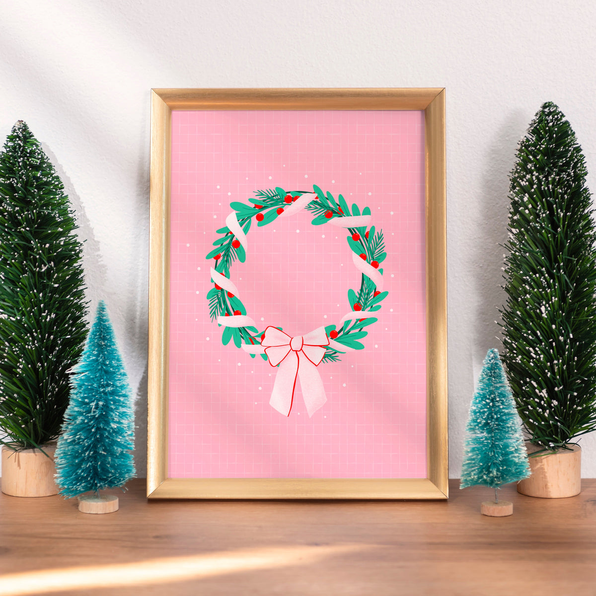A bright pink christmas print featuring an illustration of a wreath wrapped in ribbon.