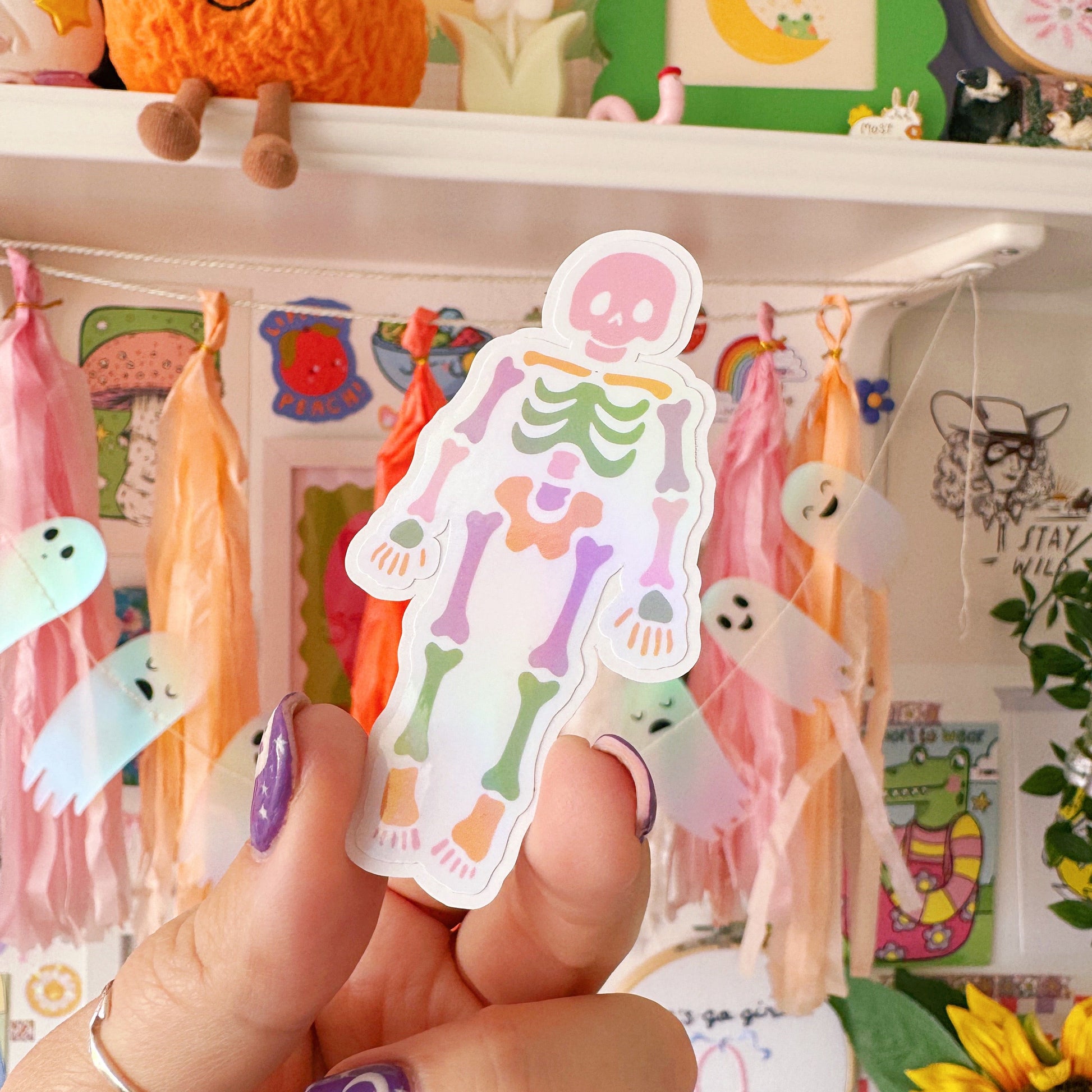 Hand holding a colourful skeleton sticker with a decorated shelf in the background