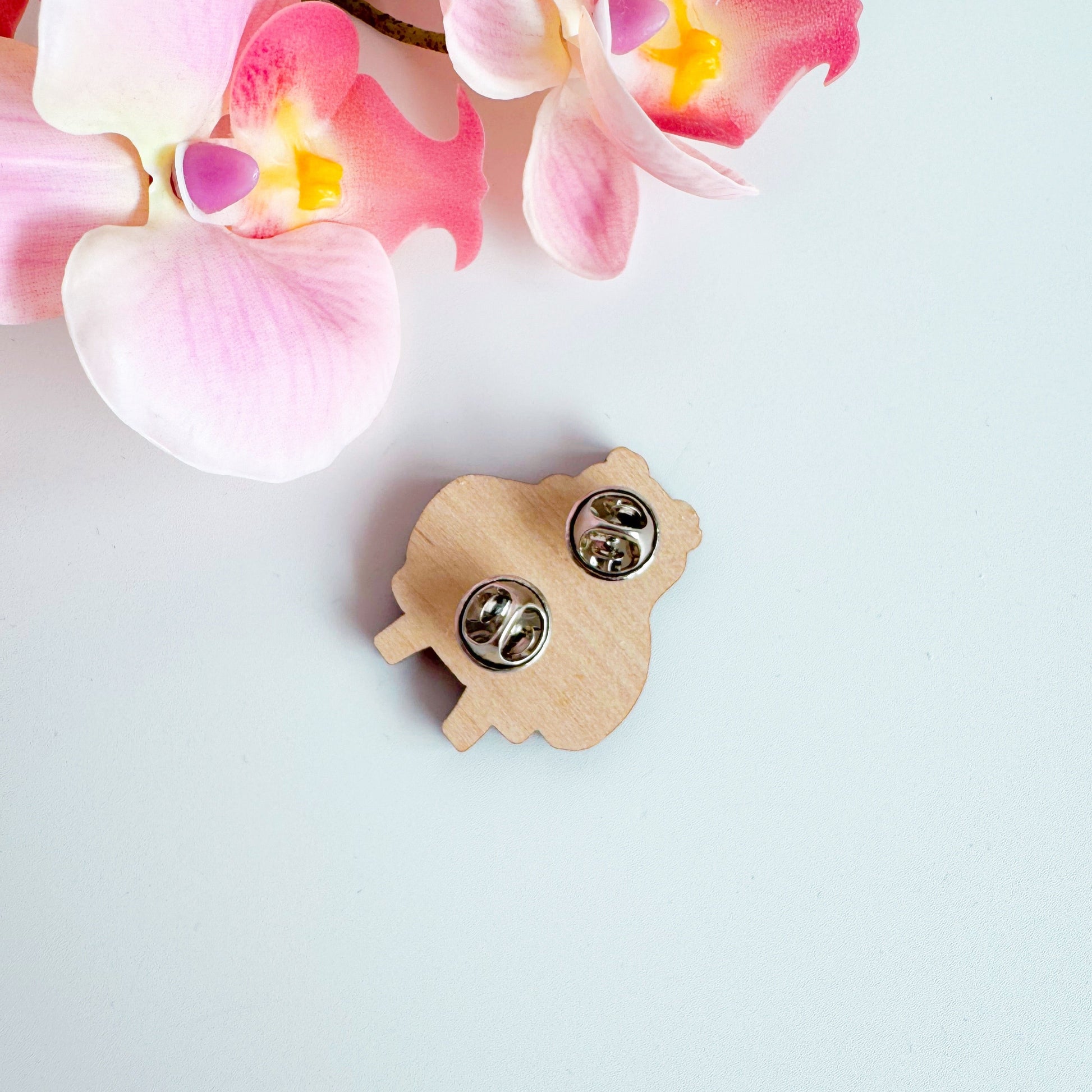 A cute illustration of a frog in sunglasses and a pink coat, holding a love heart, on an eco friendly wooden pin badge with two back fastenings.