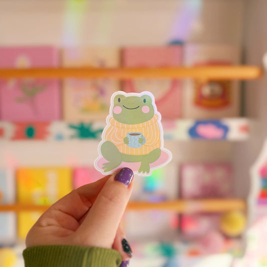Hand holding a frog sticker with a colourful background