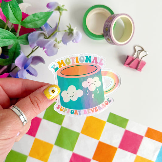 A sticker with an illustration of a mug - that has a happy cloud and a sad cloud on the front, with the words 'emotional support beverage' in colourful lettering around the mug.