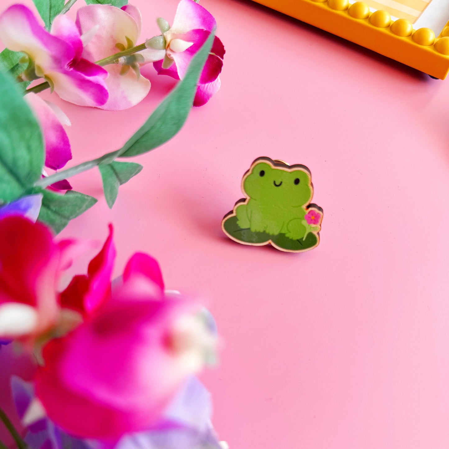 A cute green frog pin badge, made out of wood with two metal clasp fastenings to the back.