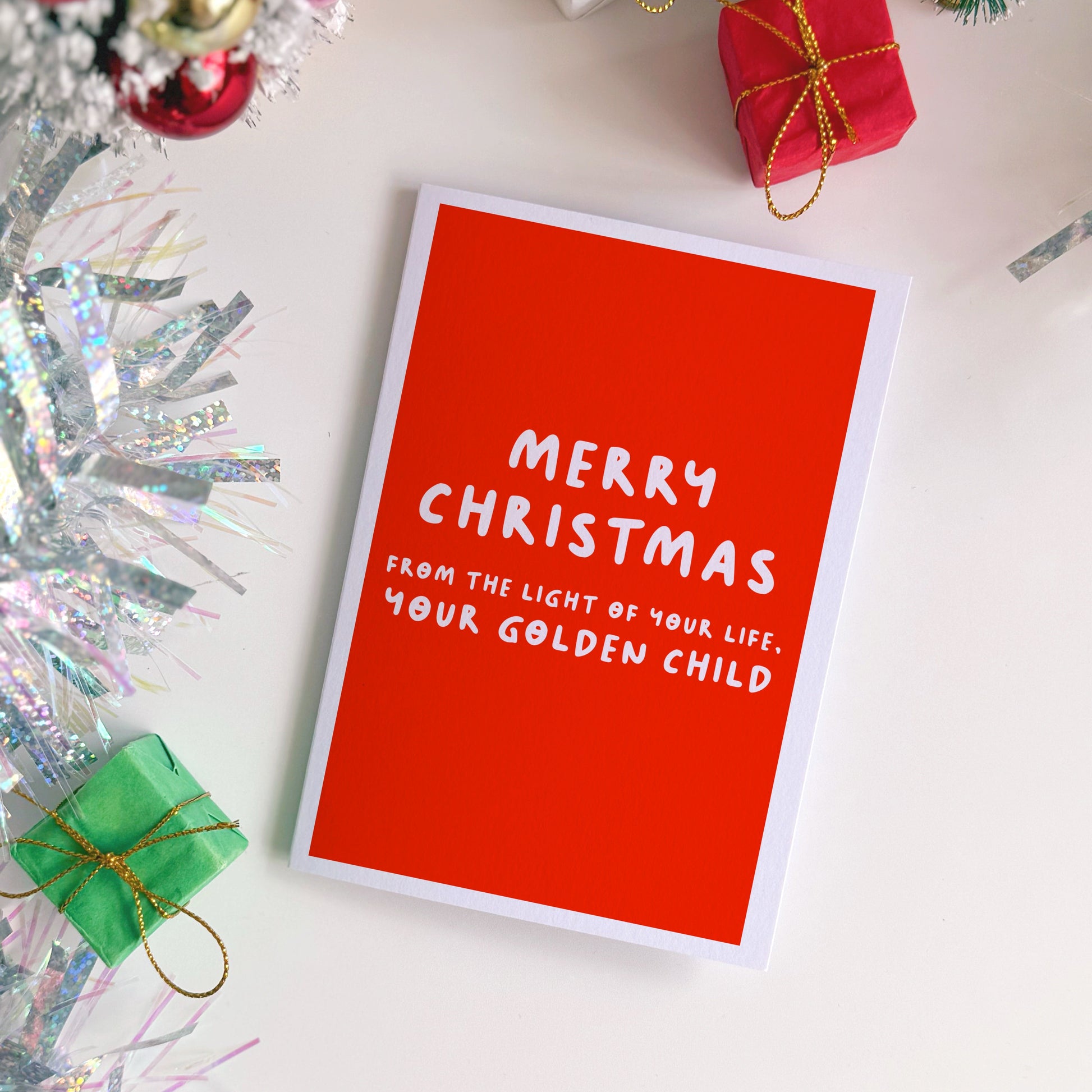 Red Christmas card with white text on a festive background with small gift boxes and decorations.
