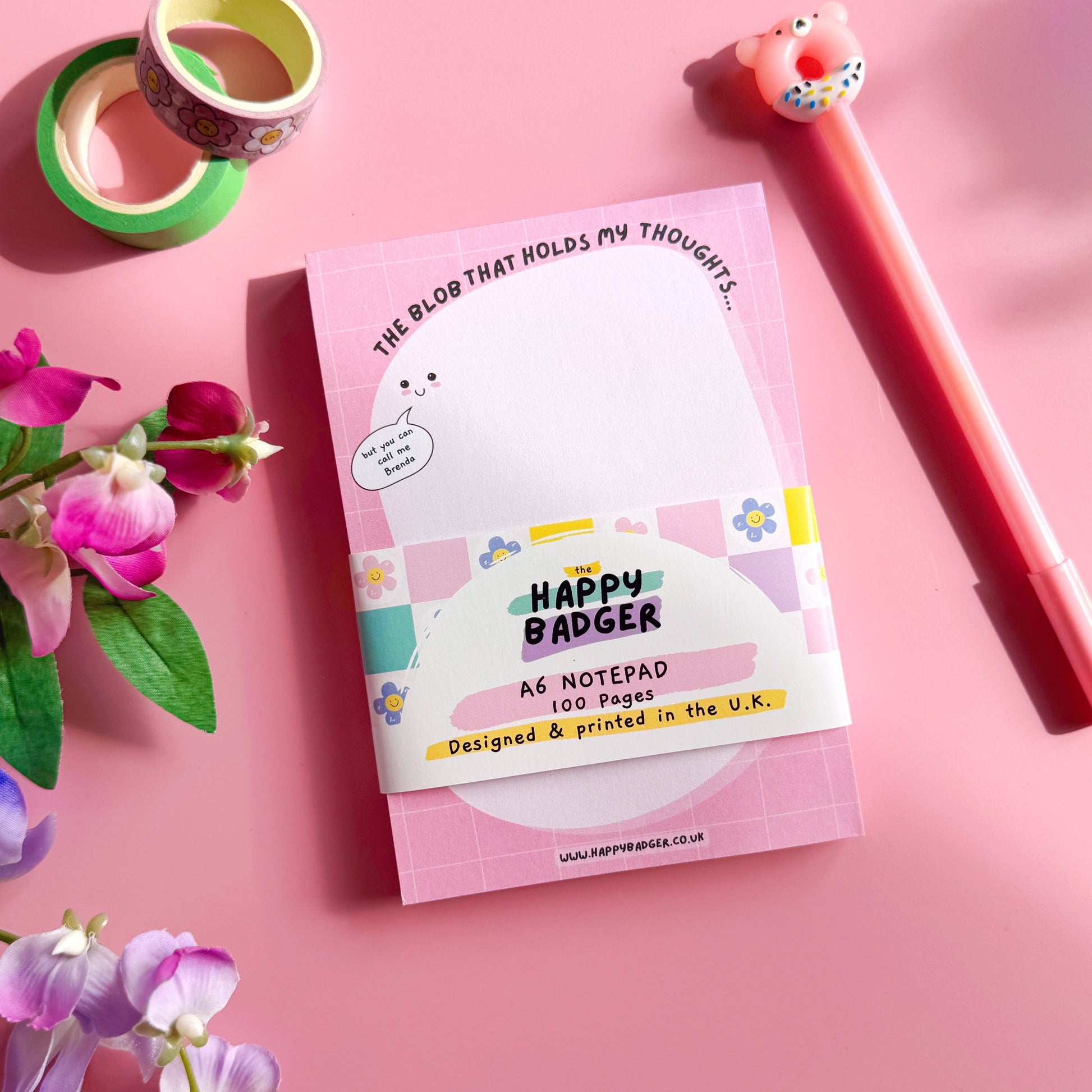 Happy Badger notebook with a pen, flowers, and tape on a pink background