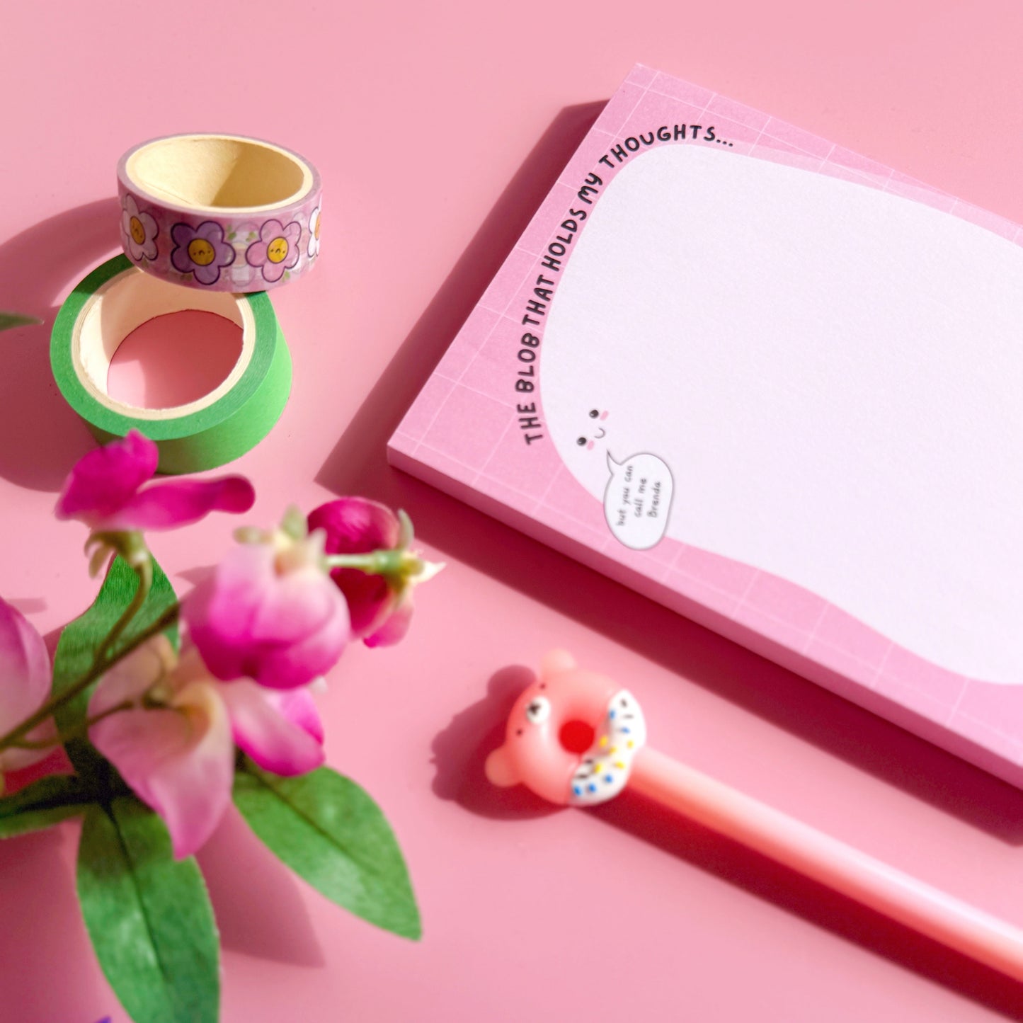 Pink notebook with a pen, flowers, and decorative items on a pink background