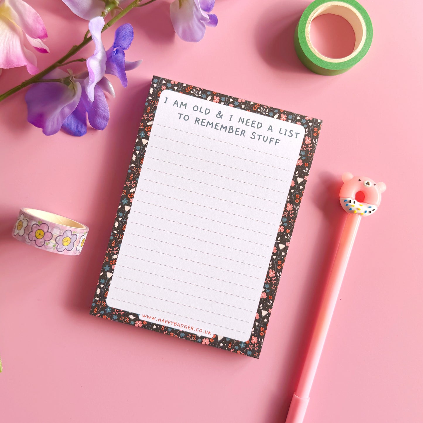 Notepad with decorative border, pen, and tape on a pink background