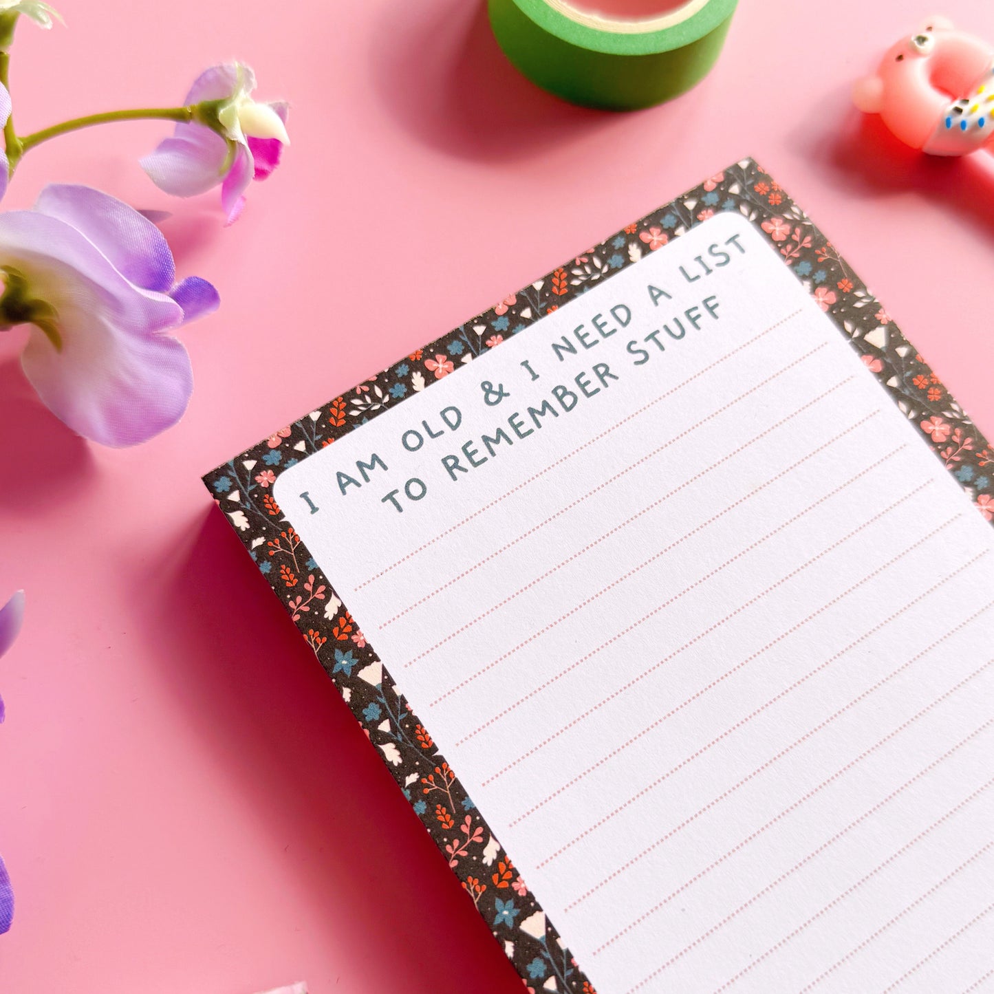 Floral notepad with humorous text on a pink background with flowers and tape.