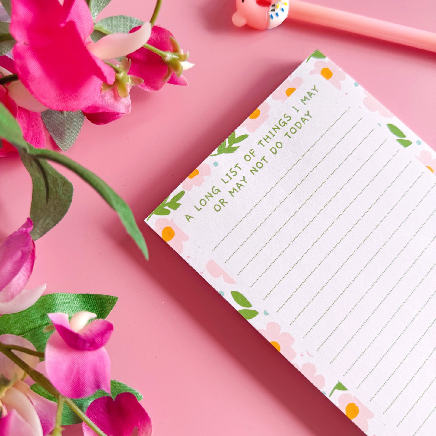 Notepad with floral design on a pink background with flowers and a pen.