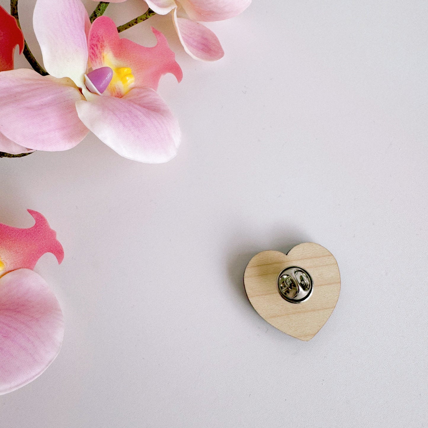 A pink heart shaped wooden pin badge, with the words 'garlic lovers club' on the front