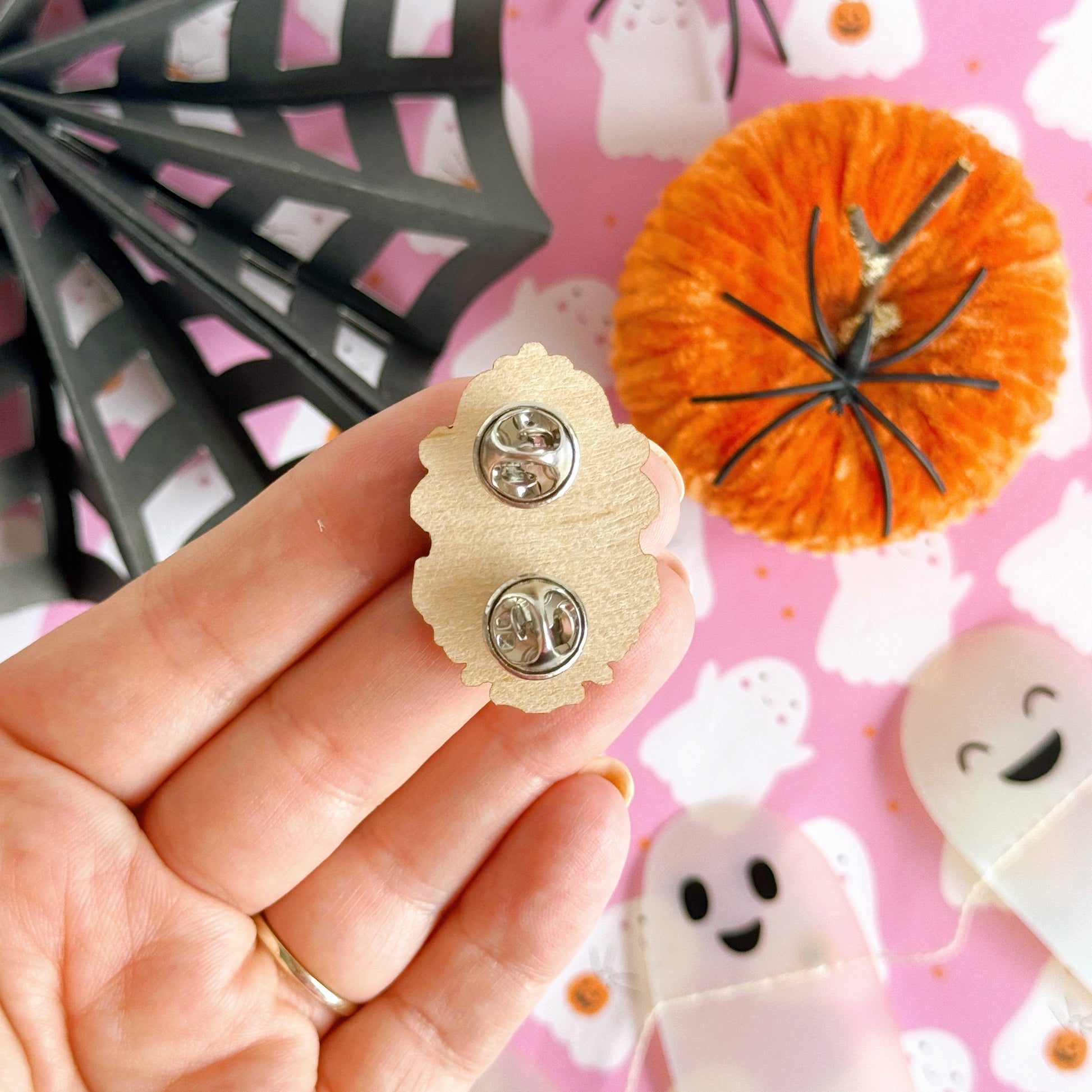 A wooden eco friendly pin badge of a cute spooky ghost on a black background, in an orange ornate frame.