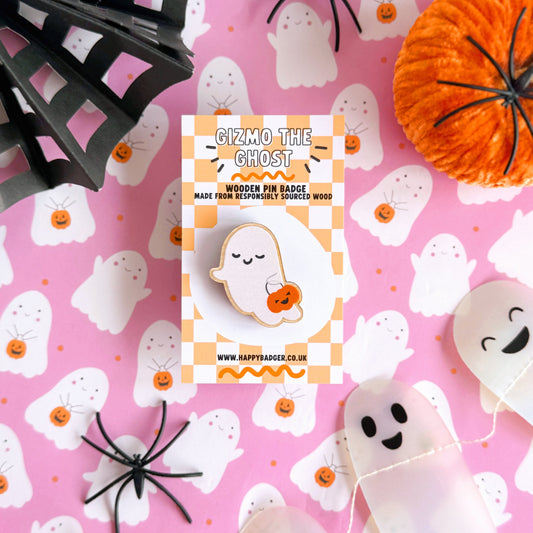 A wooden pin badge, of a cute smiling ghost, holding a trick or treating tub which is a pumpkin.