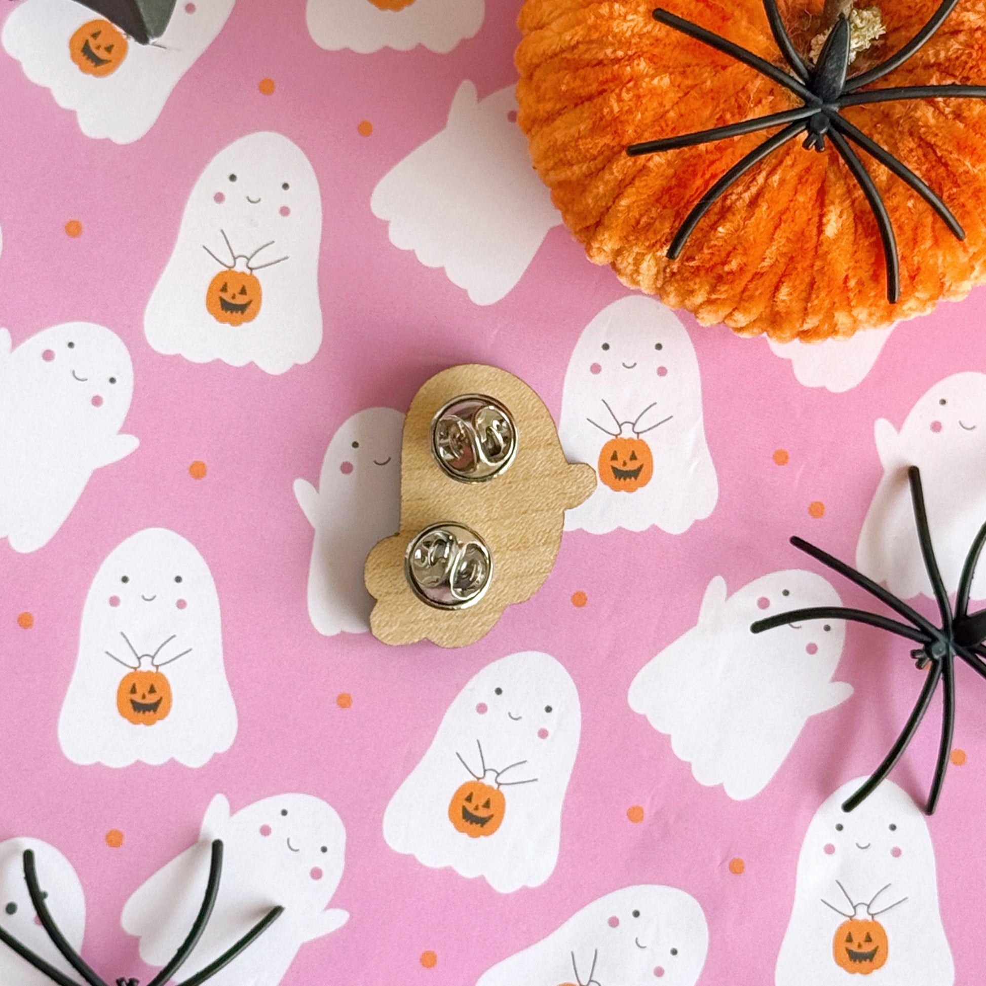 A wooden pin badge, of a cute smiling ghost, holding a trick or treating tub which is a pumpkin.