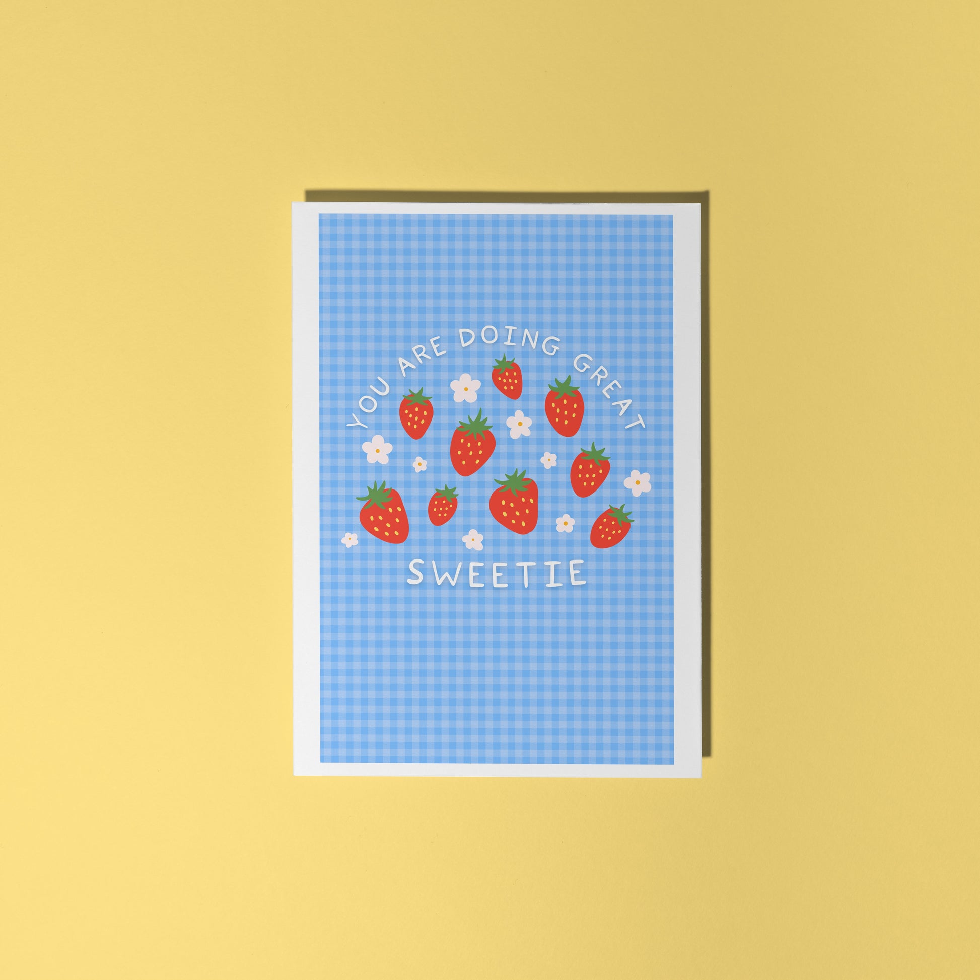 Card with strawberry design and text that reads 'you are doing great sweetie' on a blue gingham background