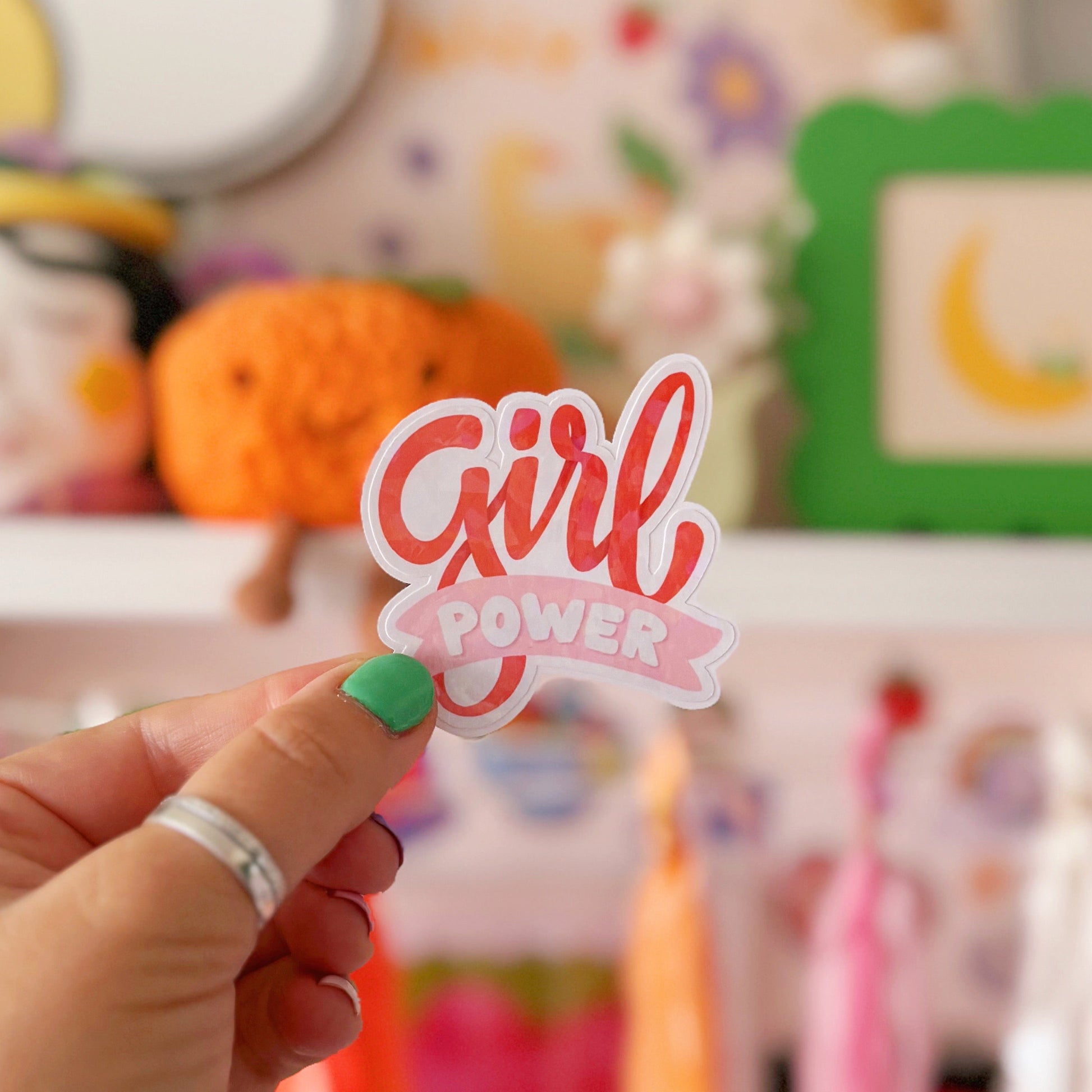 Hand holding a 'Girl Power' sticker in front of colorful decorations