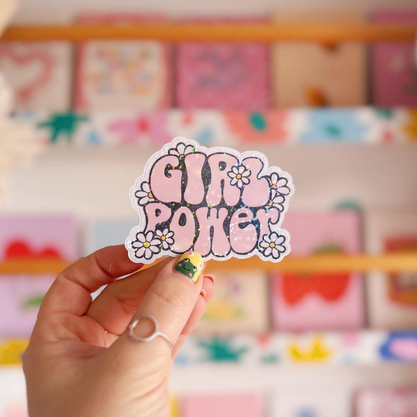 Hand holding a 'Girl Power' sticker in front of a colourful display