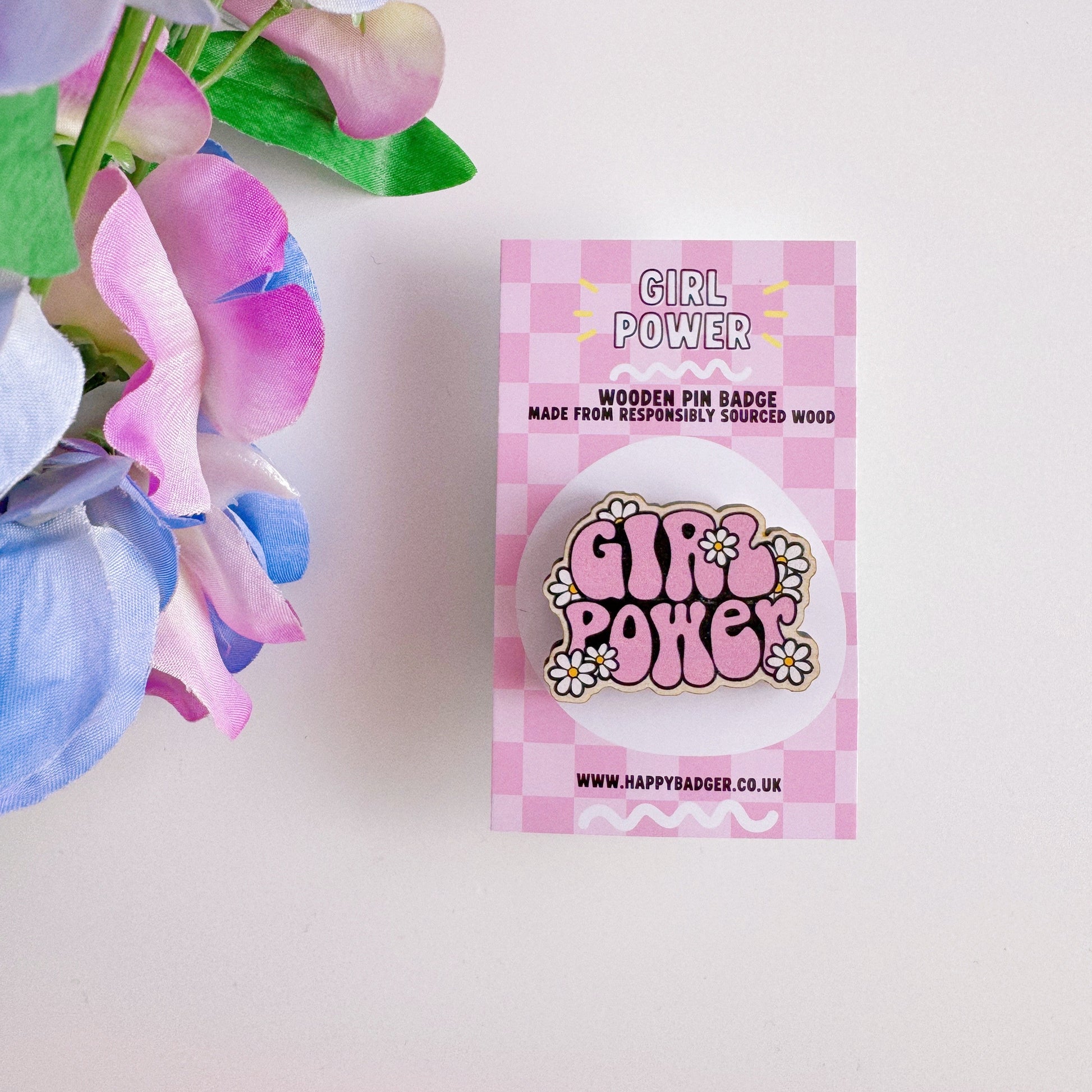 A pink wooden pin badge with the words girl power on, surrounded by white daisies.