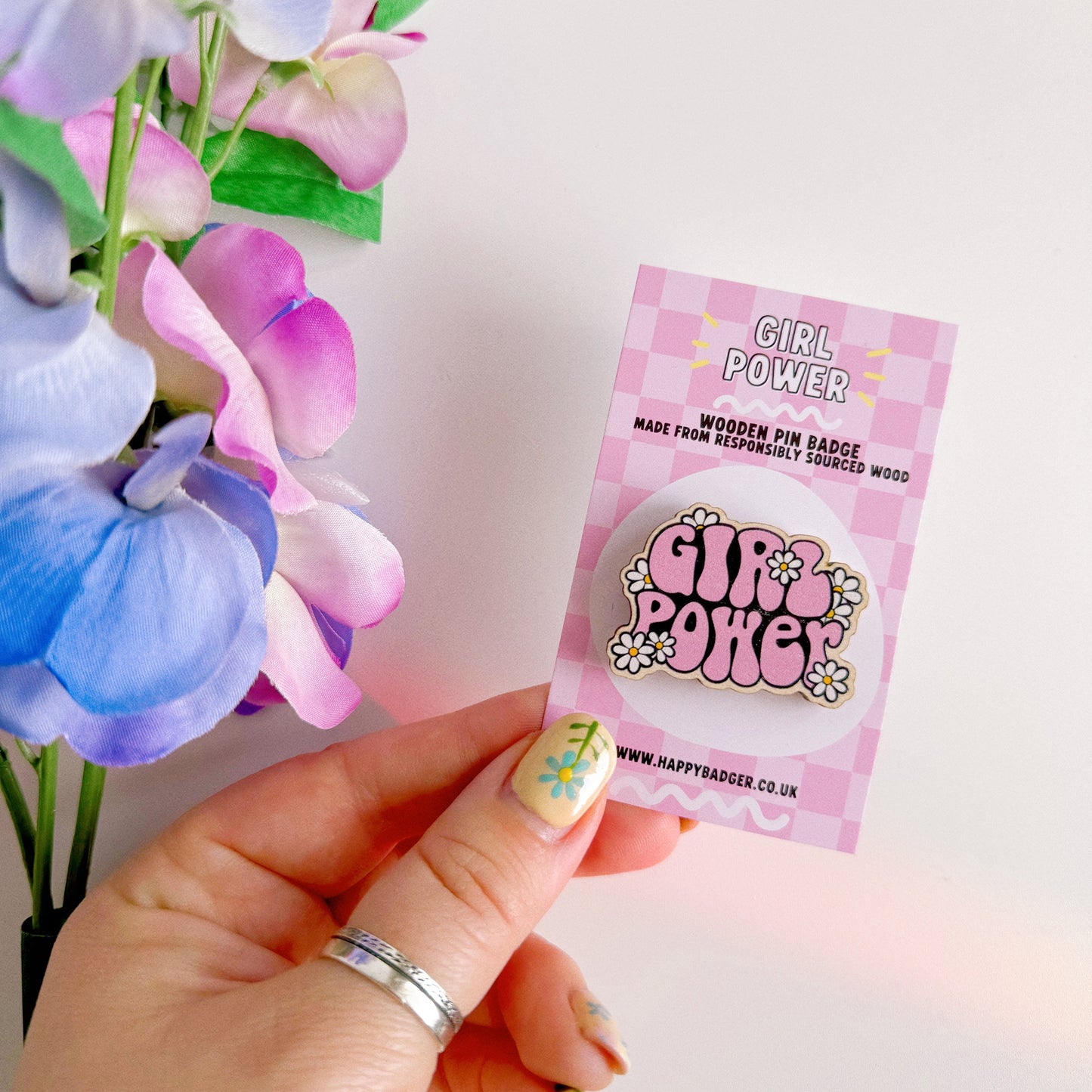 A pink wooden pin badge with the words girl power on, surrounded by white daisies.