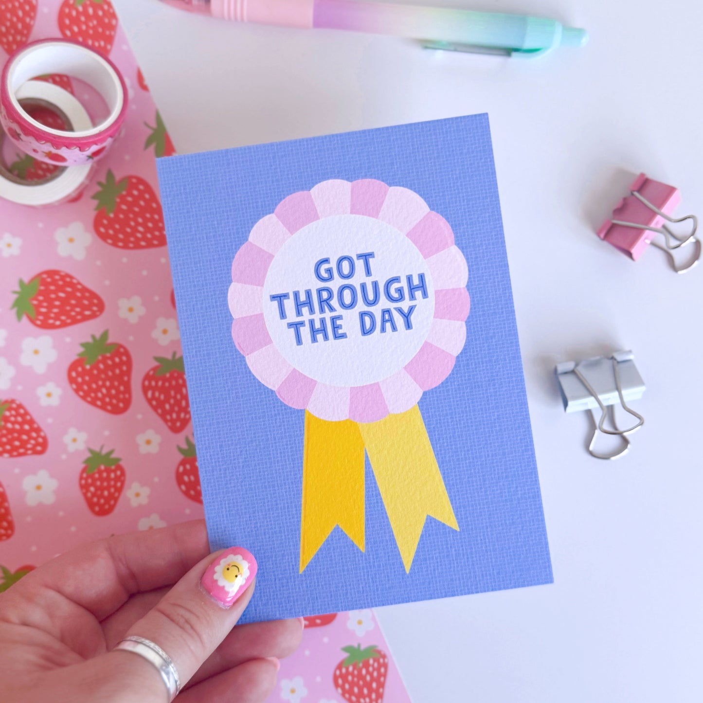A blue postcard, with a rosette in pink and yellow, saying got through the day.
