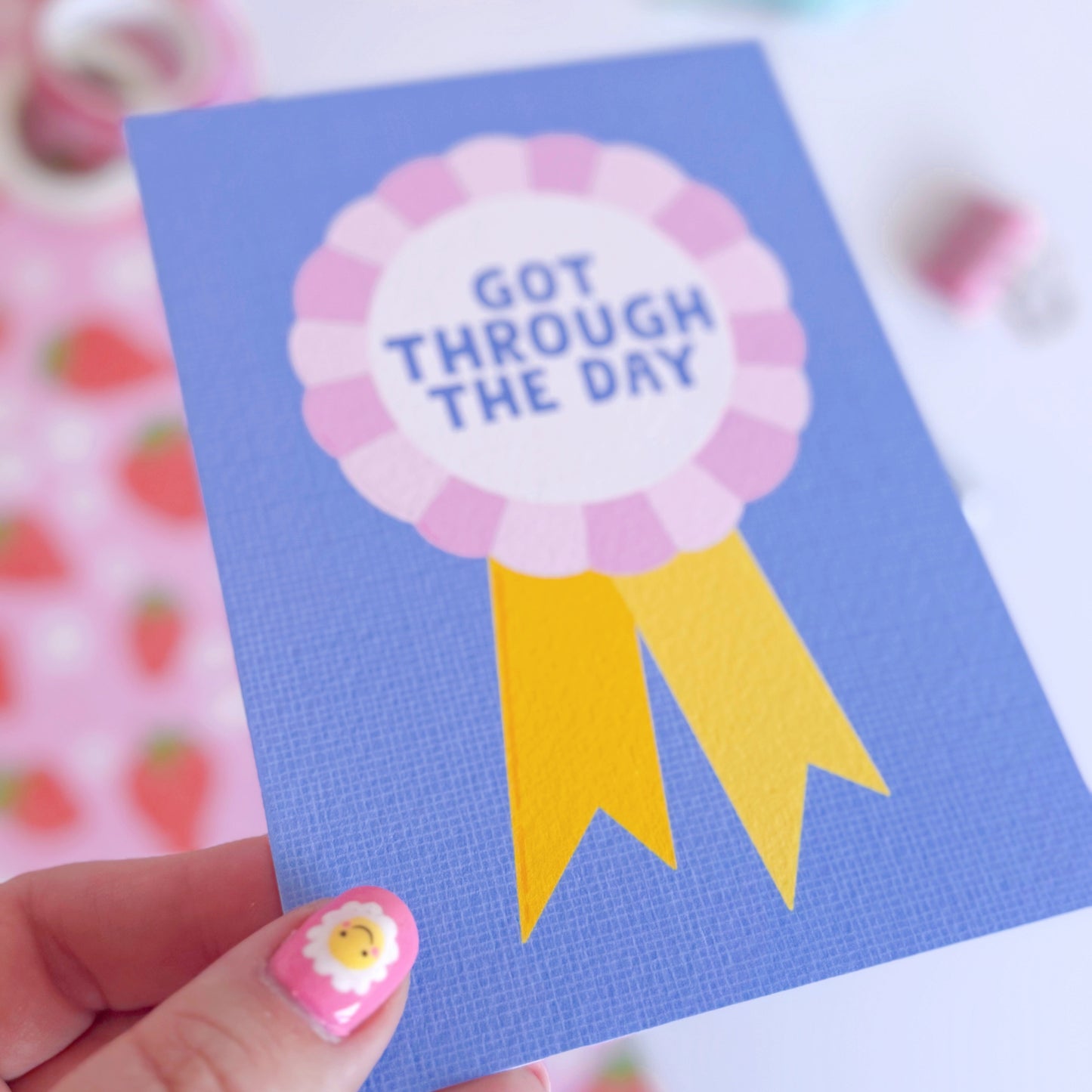 A blue postcard, with a rosette in pink and yellow, saying got through the day.