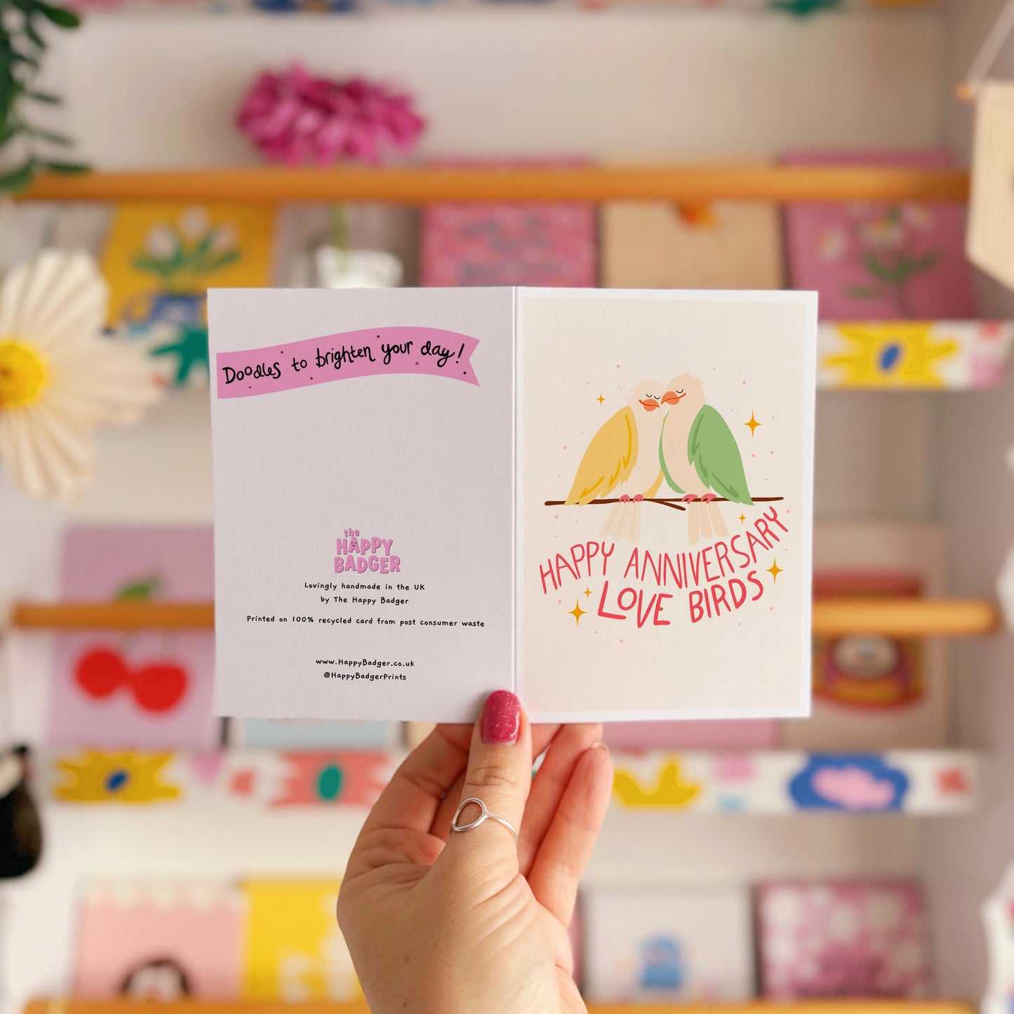 An illustrated anniversary card with two birds sitting on a branch, looking loved up. The hand written lettering underneath them reads ;happy anniversary love birds'.