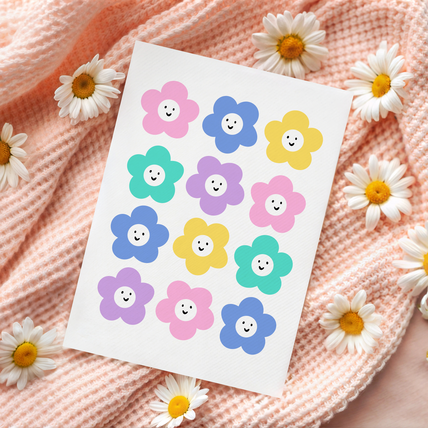 A white card with 12 colourful smiling daisy-like flowers on the front.