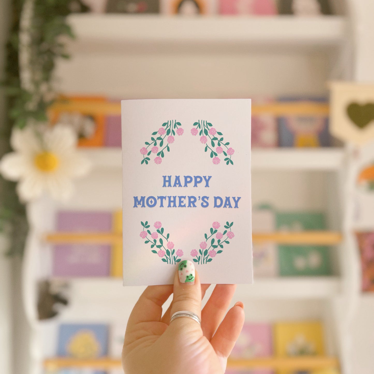 A Mother's Day card, with a pink and green floral border and the words 'Happy Mother's Day' written in the centre in blue.