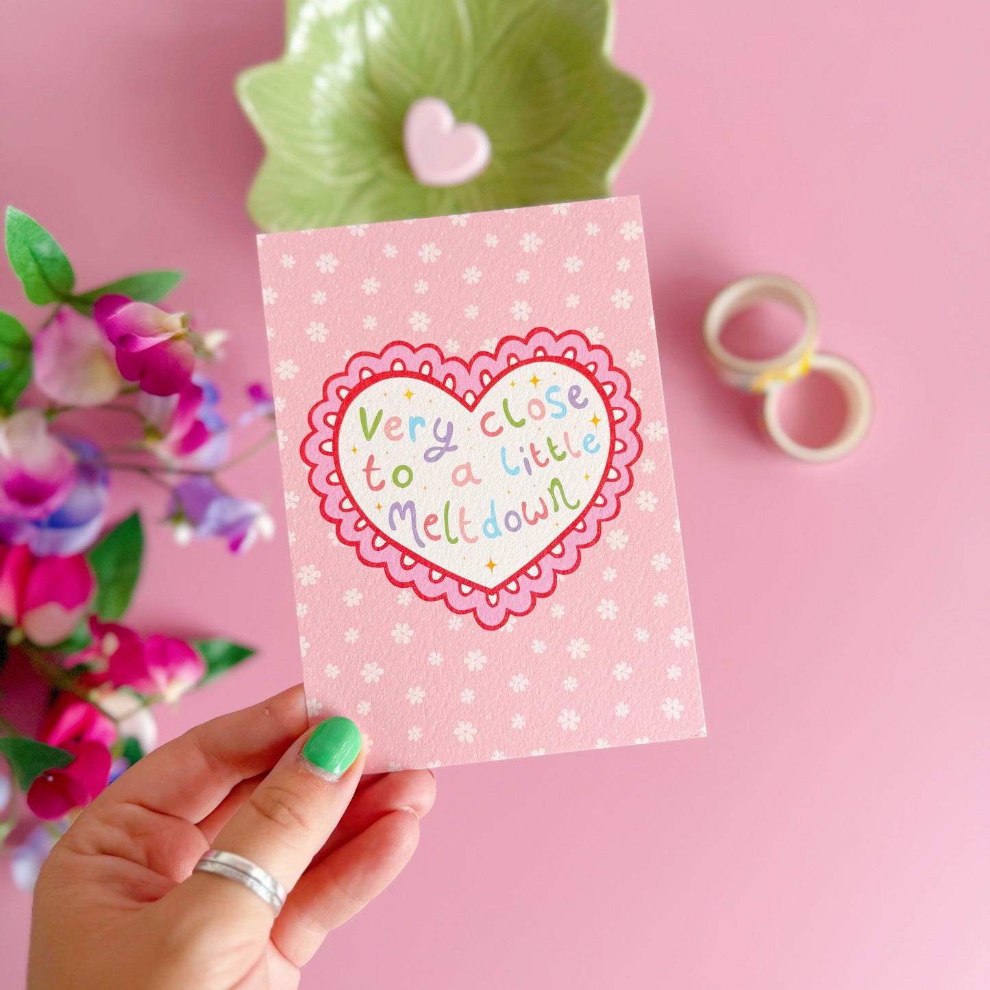 Hand holding a pink card with a heart design on a pink background