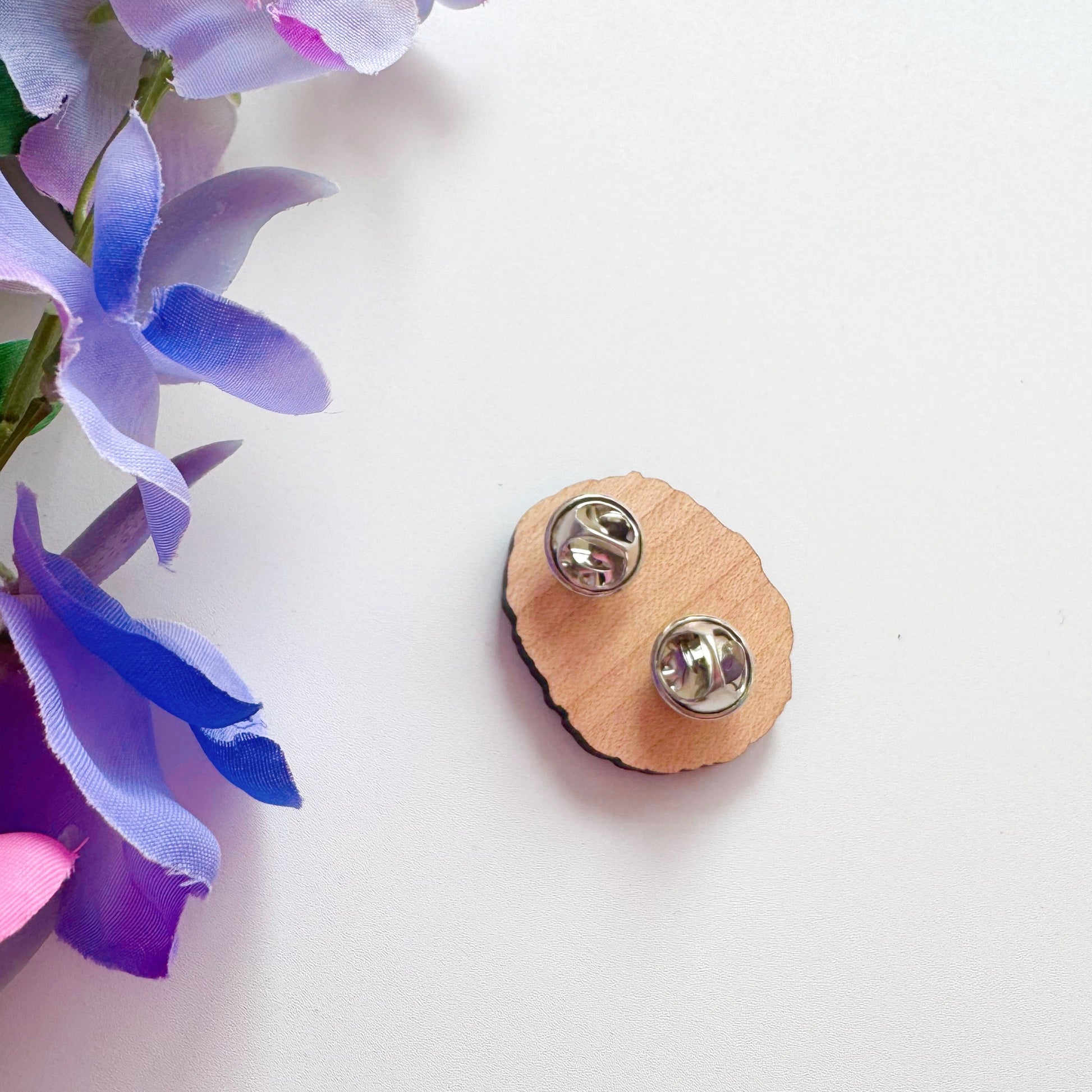 A wooden pin badge featuring a cute hedgehog curled up in a ball, with a little smiling face, holding a red strawberry in her arms.